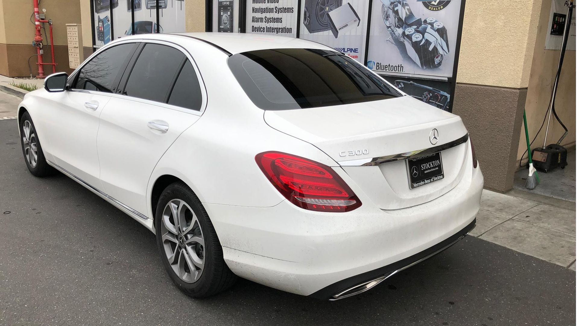 White sedan parked outside a storefront, viewed from the rear-left side