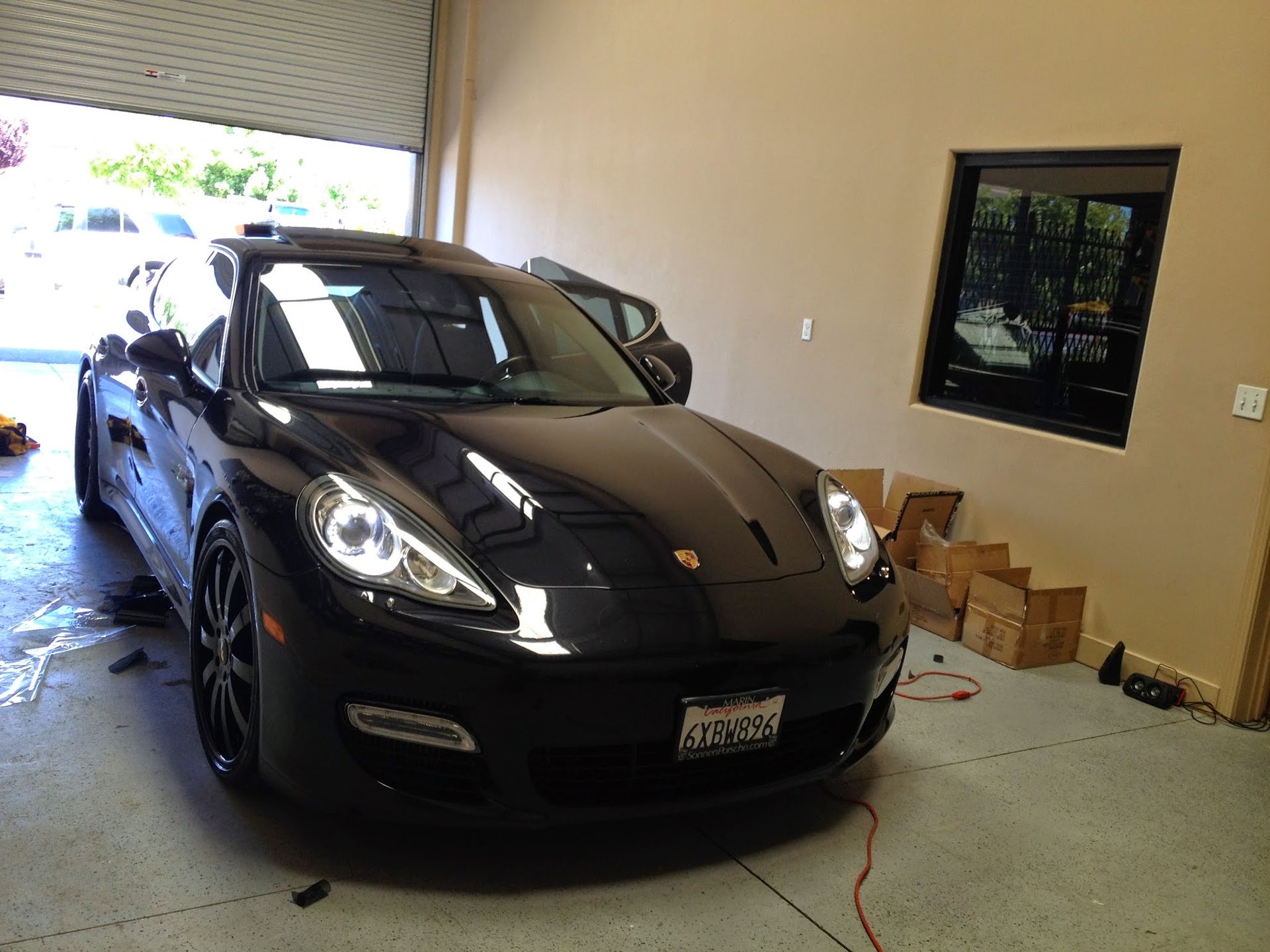 Black Porsche sports car parked indoors beside a wall and boxes.