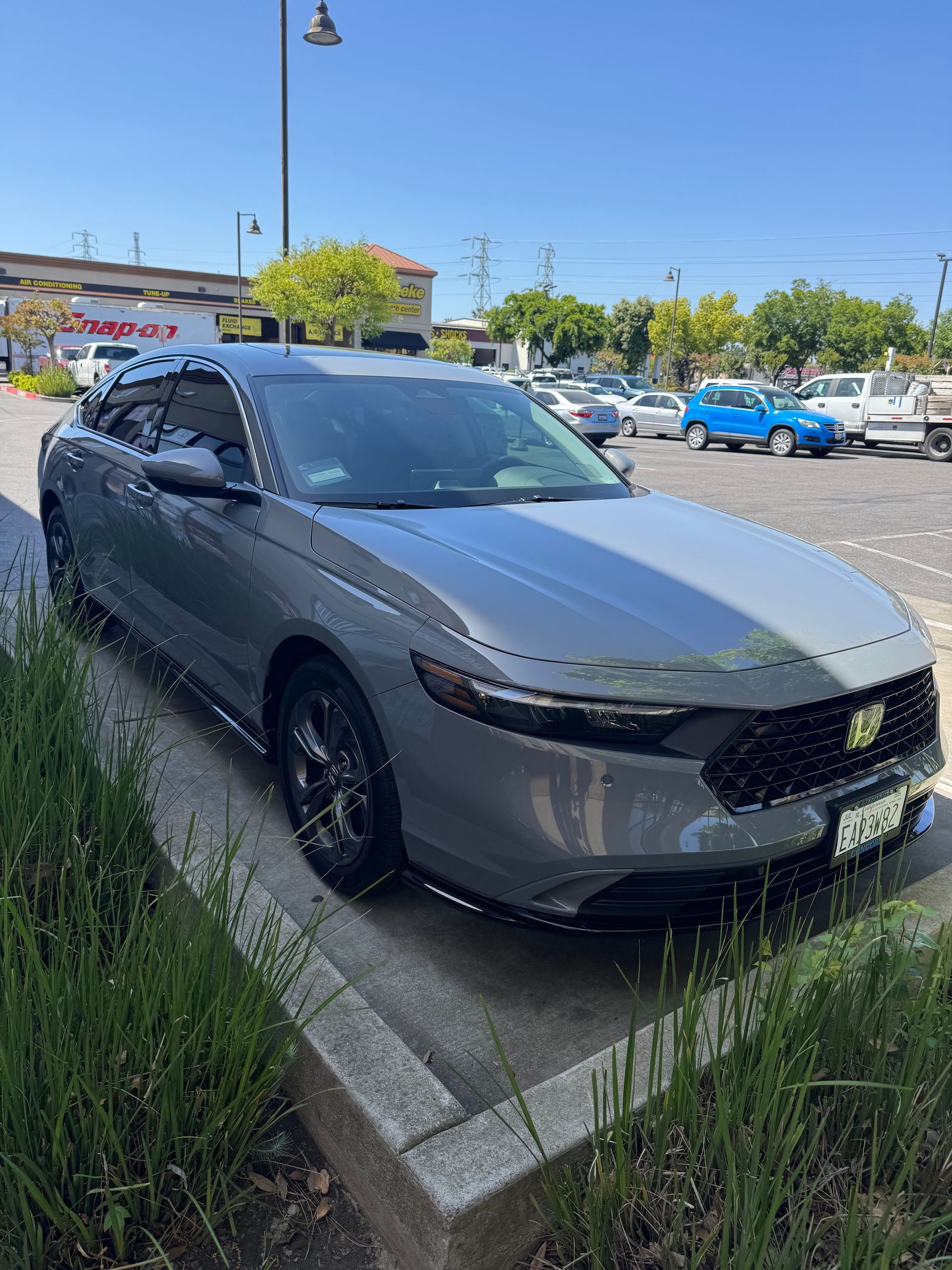 Gray SUV parked on a curb in a sunny parking lot, with other cars and trees in the background.