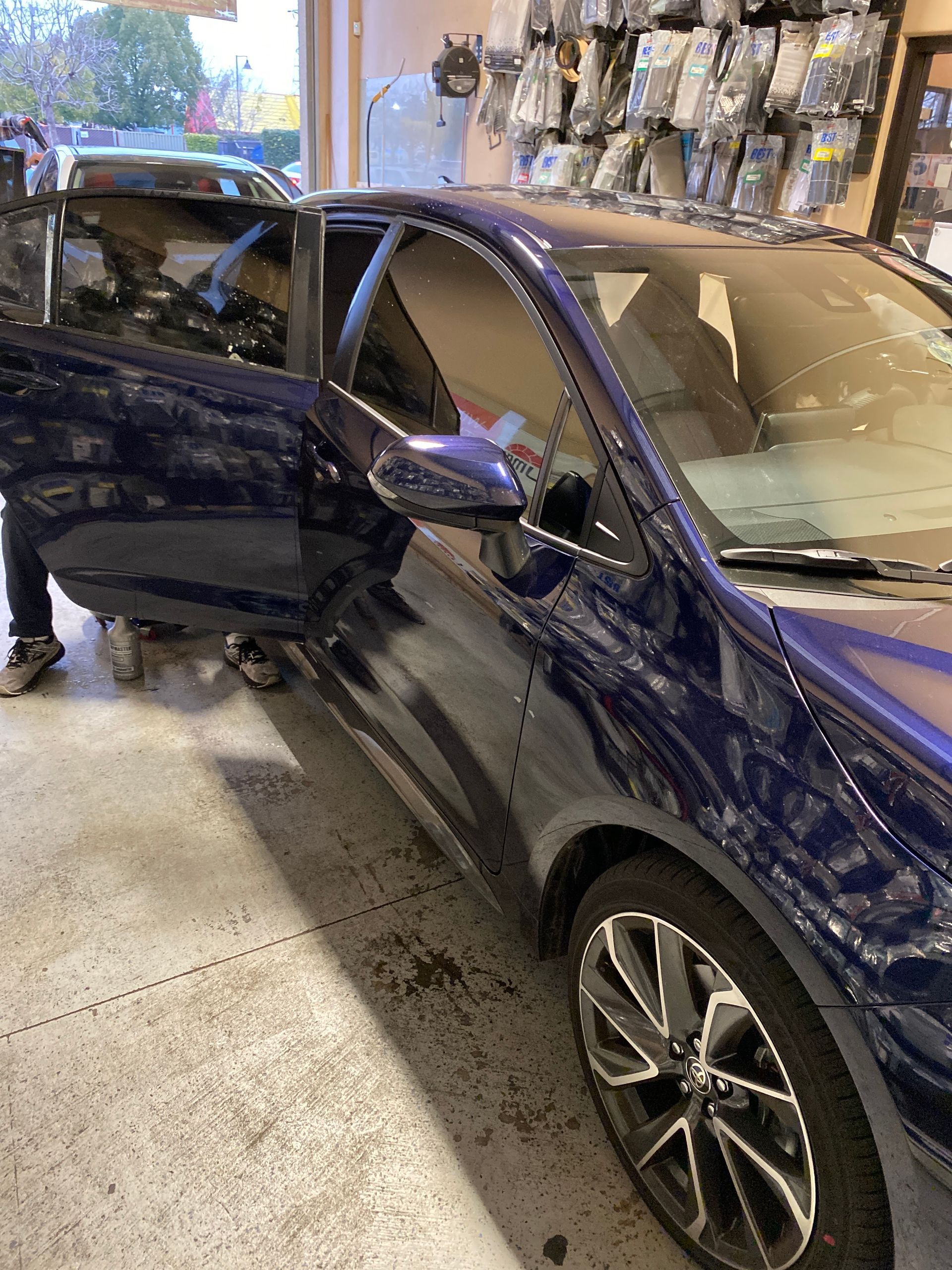 Blue car with front passenger door open inside an auto shop, showing visible damage to the front side.