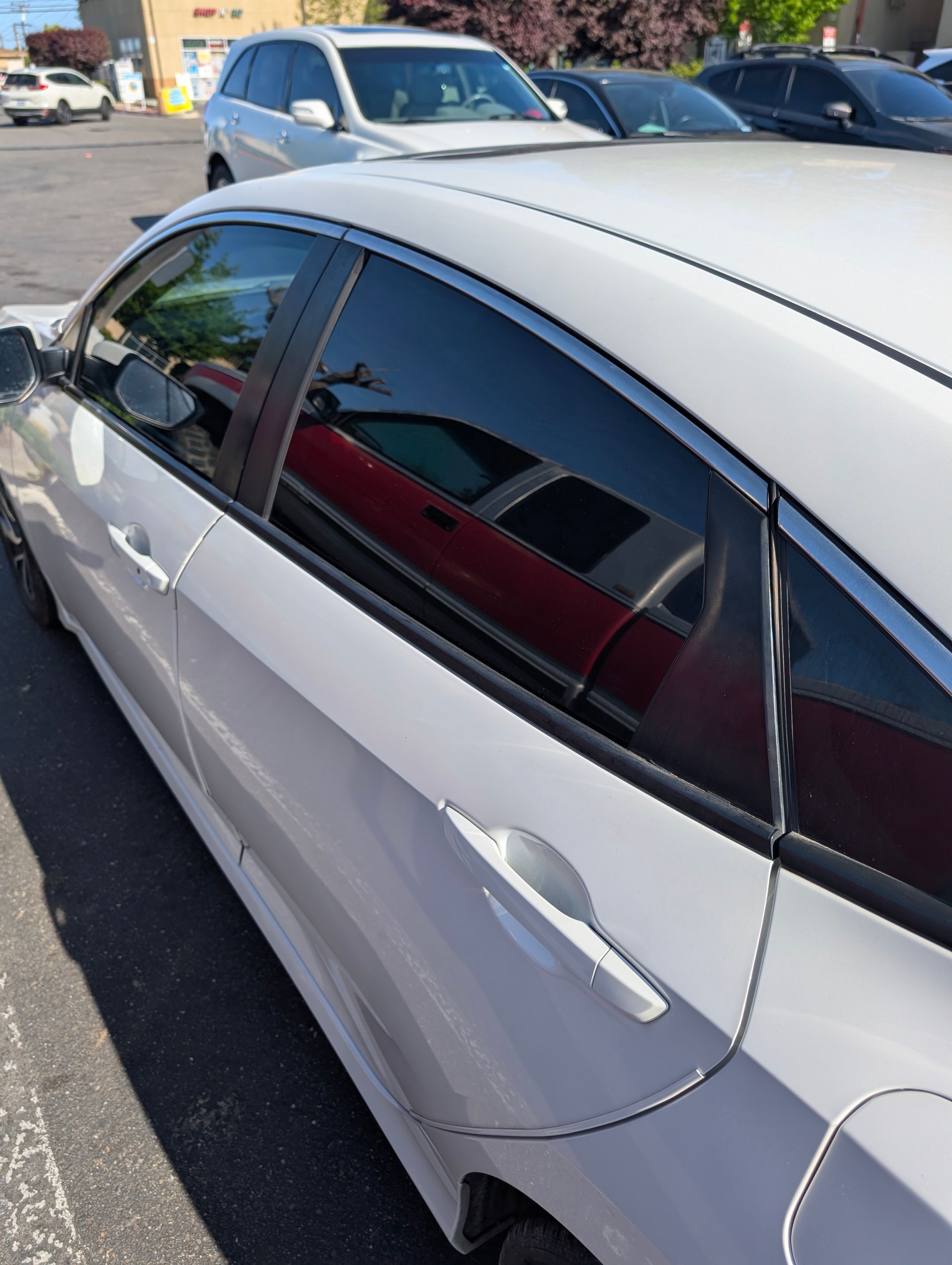 White sedan parked in a lot, showing the side windows and doors in sunlight