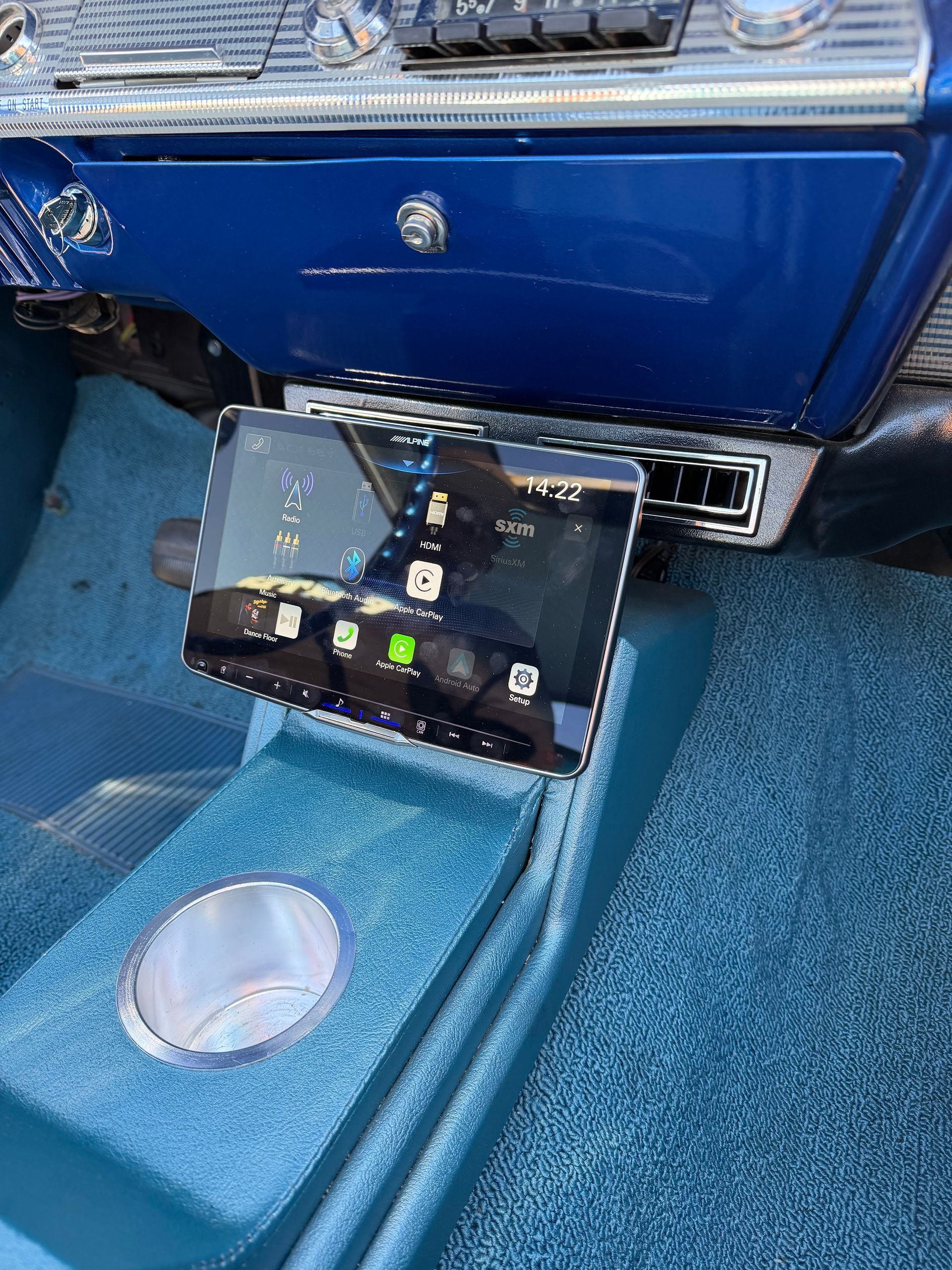 Blue car interior with a dashboard-mounted screen above the center console and a cup holder below