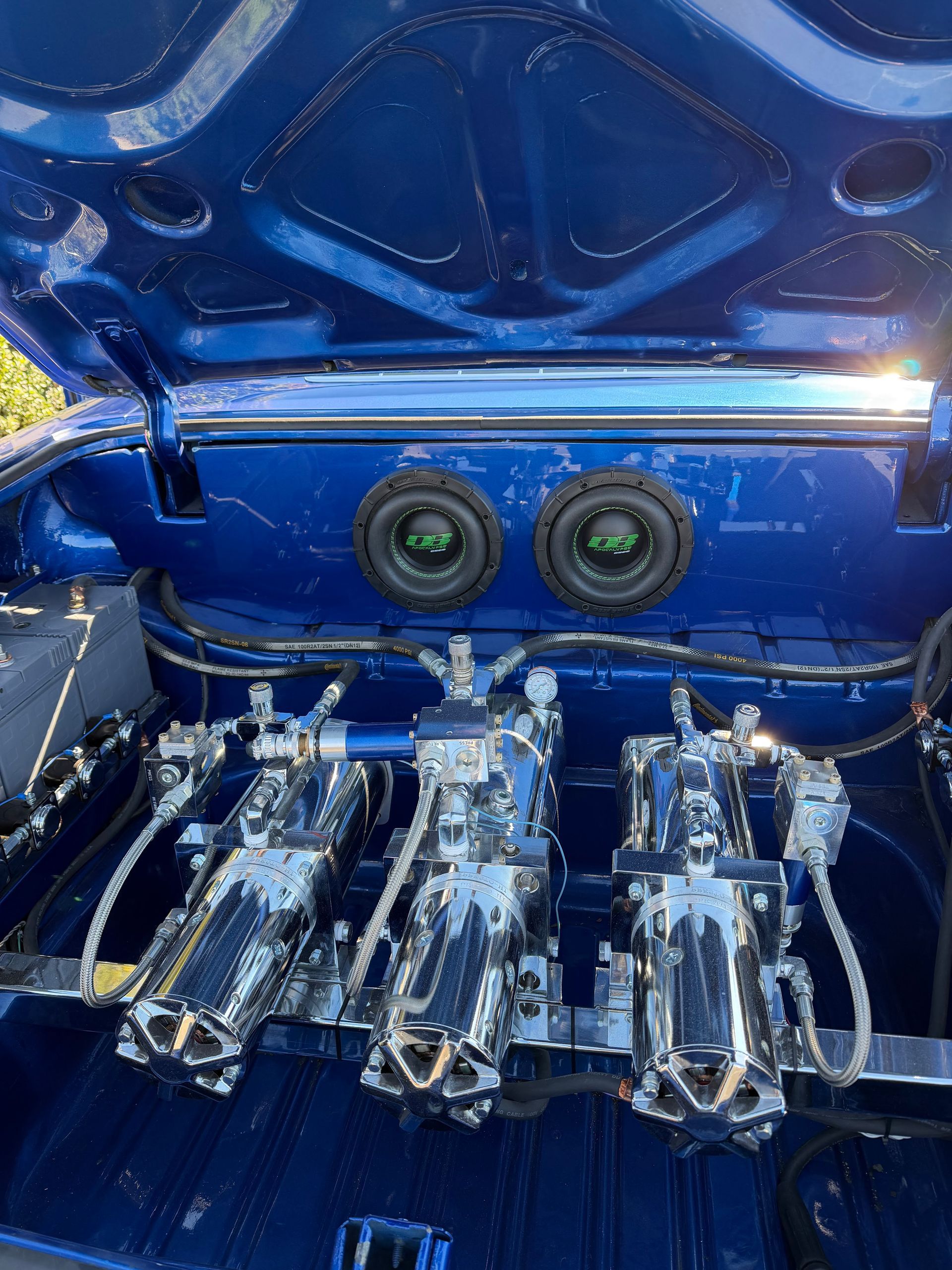 Blue car audio setup with multiple amplifiers and two subwoofers mounted under an open trunk lid