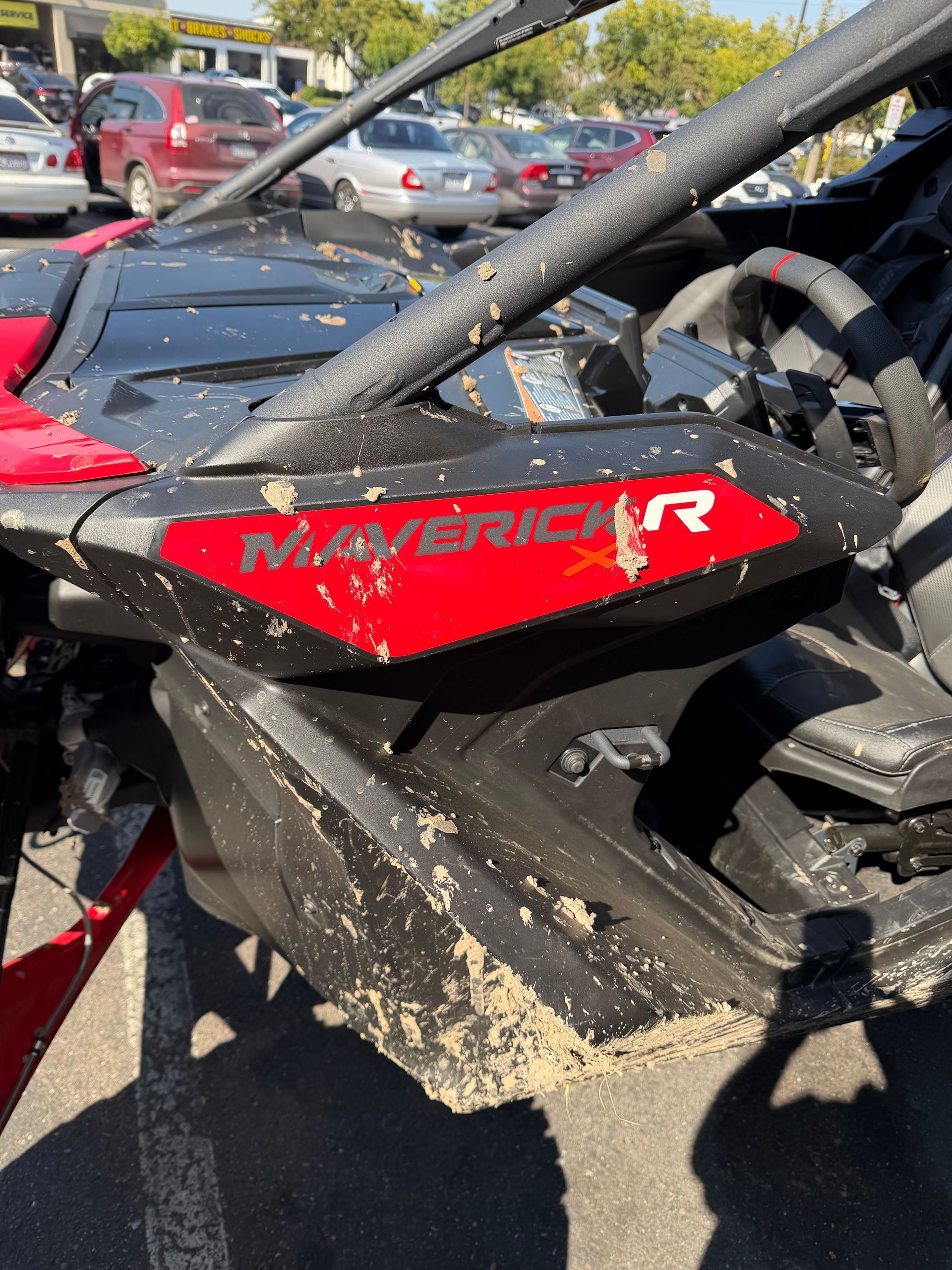 Mud-splattered red and black Maverick X3 off-road vehicle parked outdoors