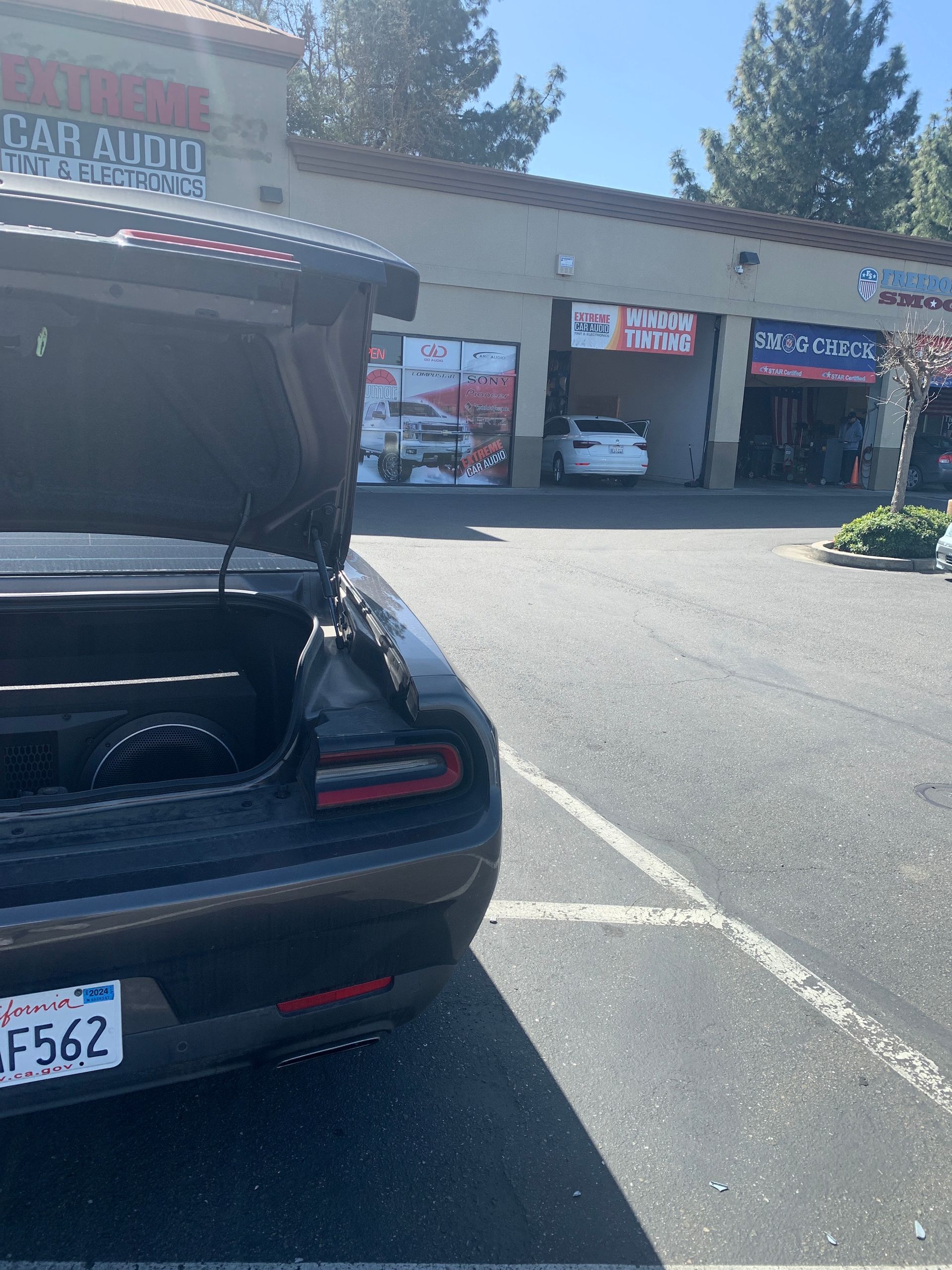 Black sports car with trunk open in a parking lot outside a strip mall on a sunny day
