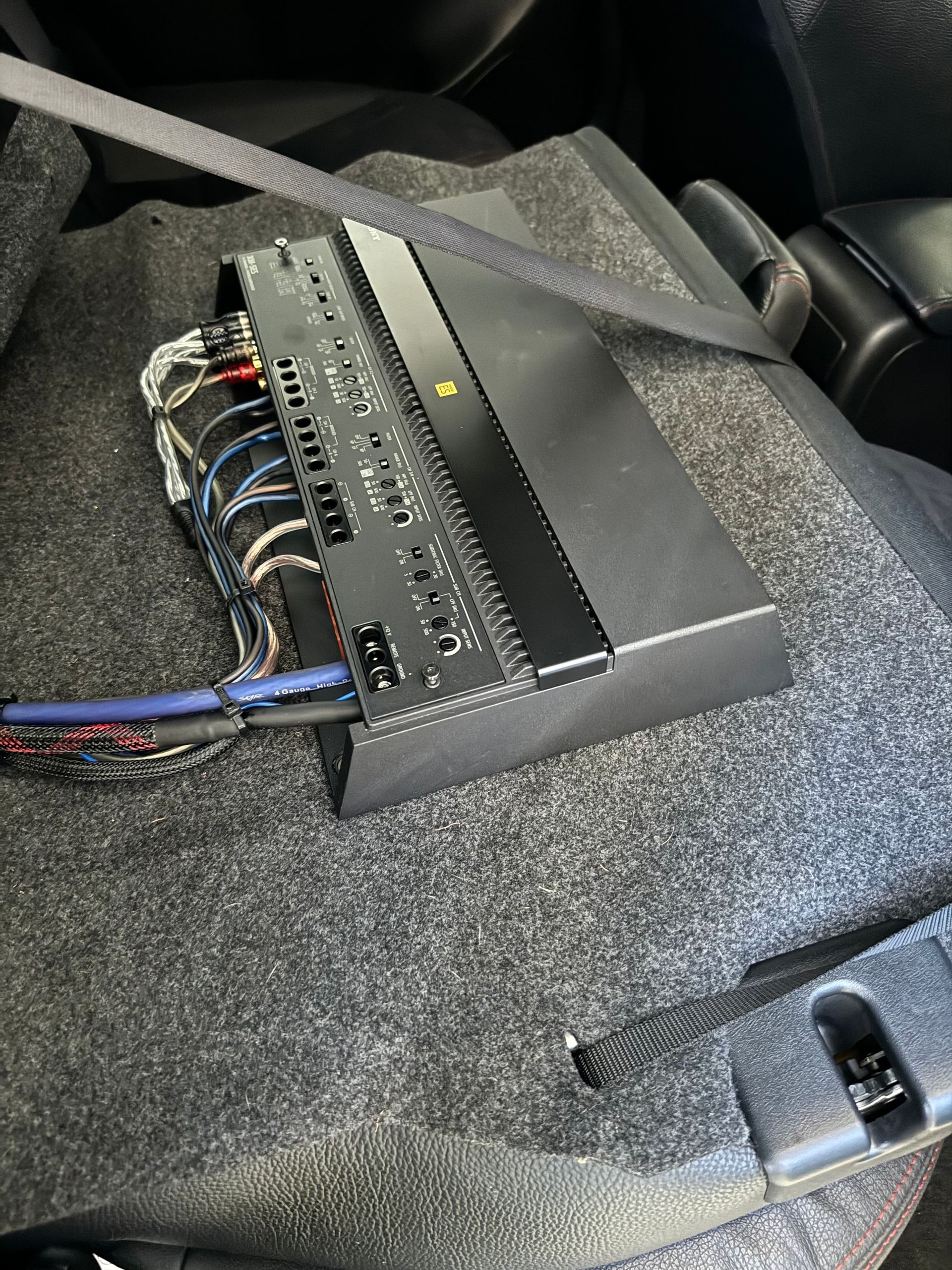 Black electronic module with wires mounted on carpeted car floor near a seatbelt buckle