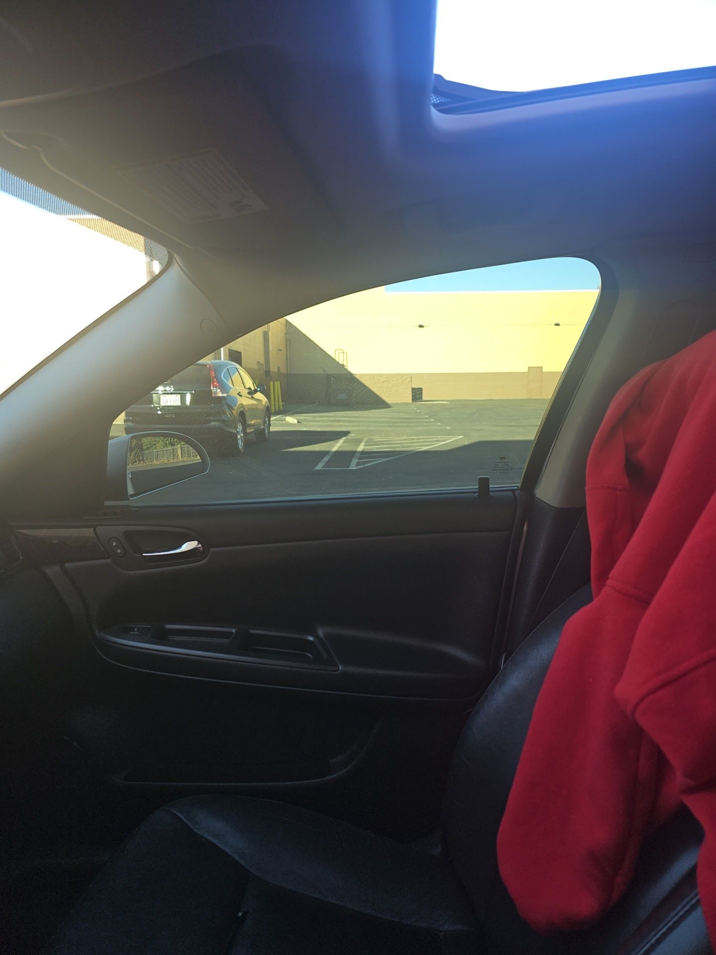 Car interior with a red jacket on the passenger seat, parked beside a beige building in daylight.