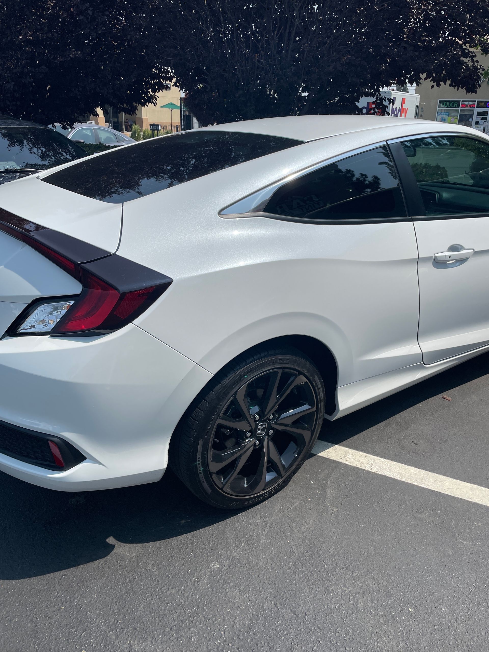 White coupe parked in a lot, shown from the rear side with black wheels and tinted windows