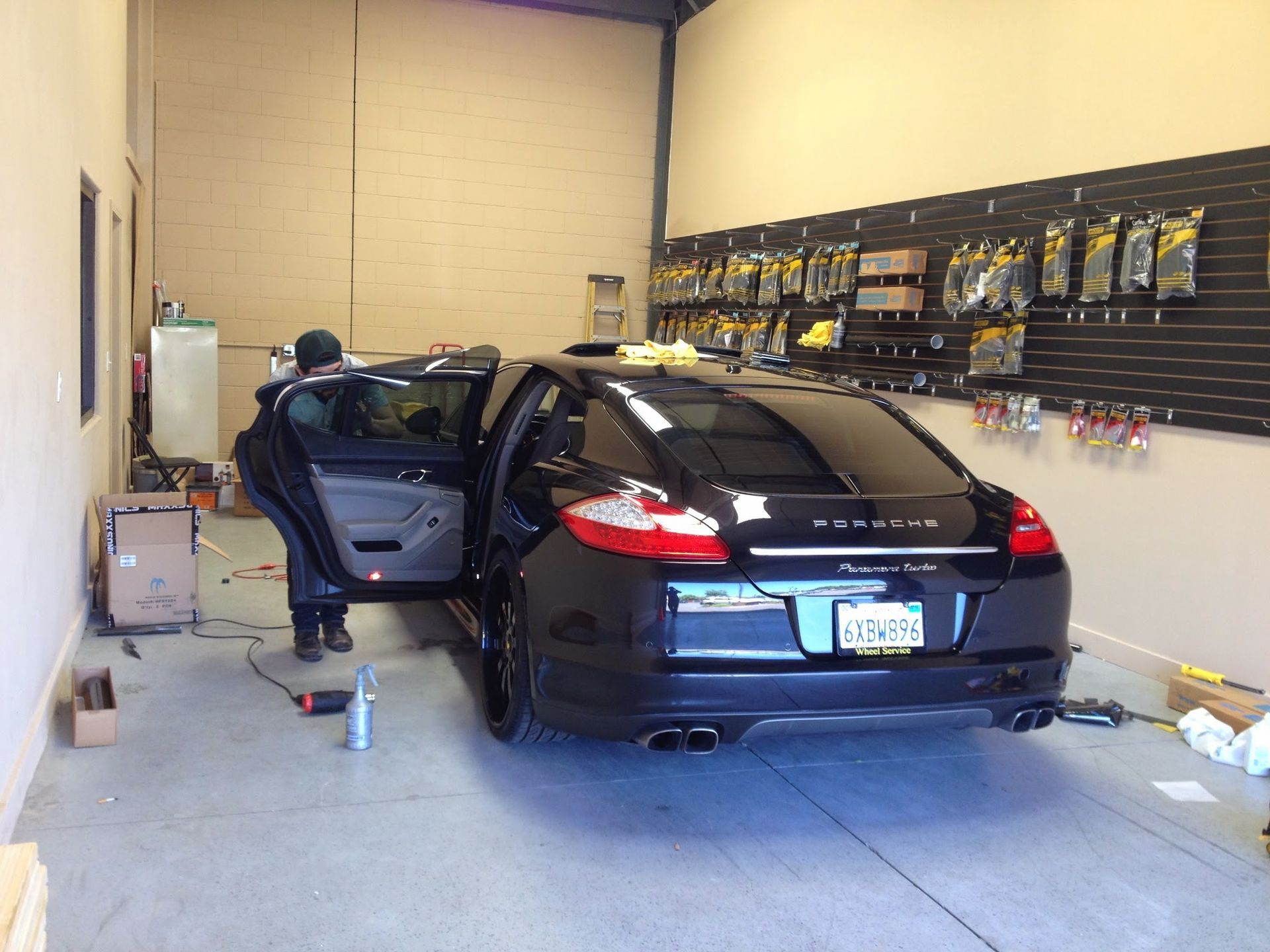 Black sedan in a garage with the rear door open, surrounded by tools and equipment.