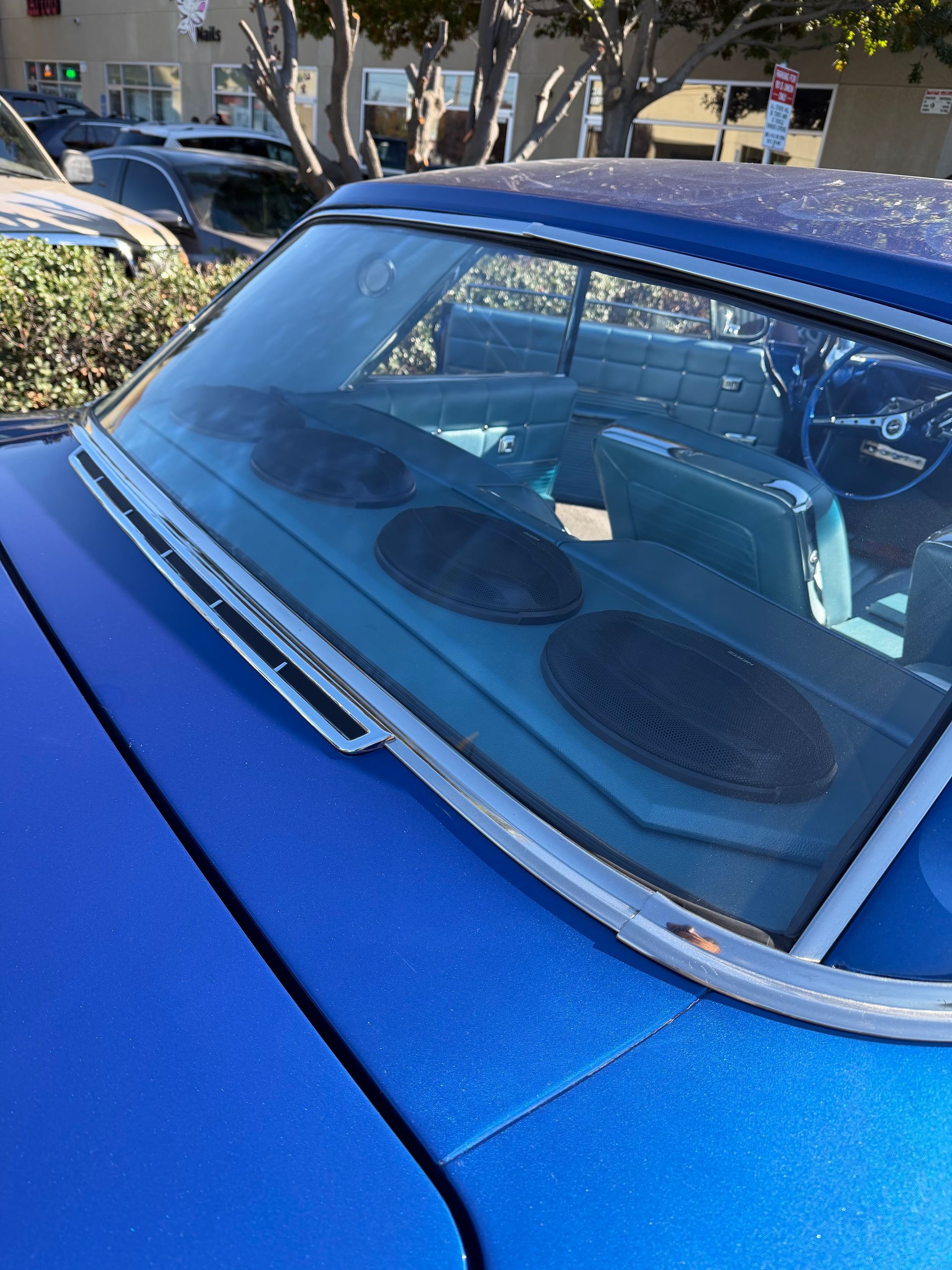 Blue car windshield and dashboard with dashboard speakers, parked outdoors in sunlight