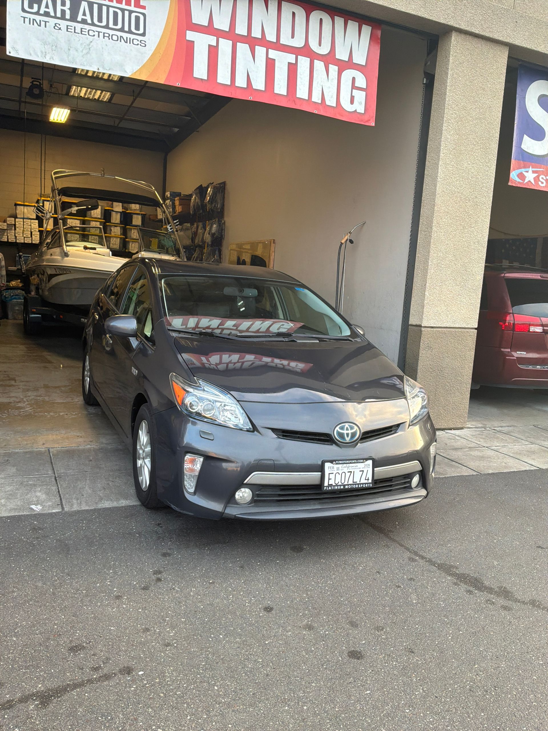 Gray Toyota Prius parked outside a window tinting shop with a large red sign above it