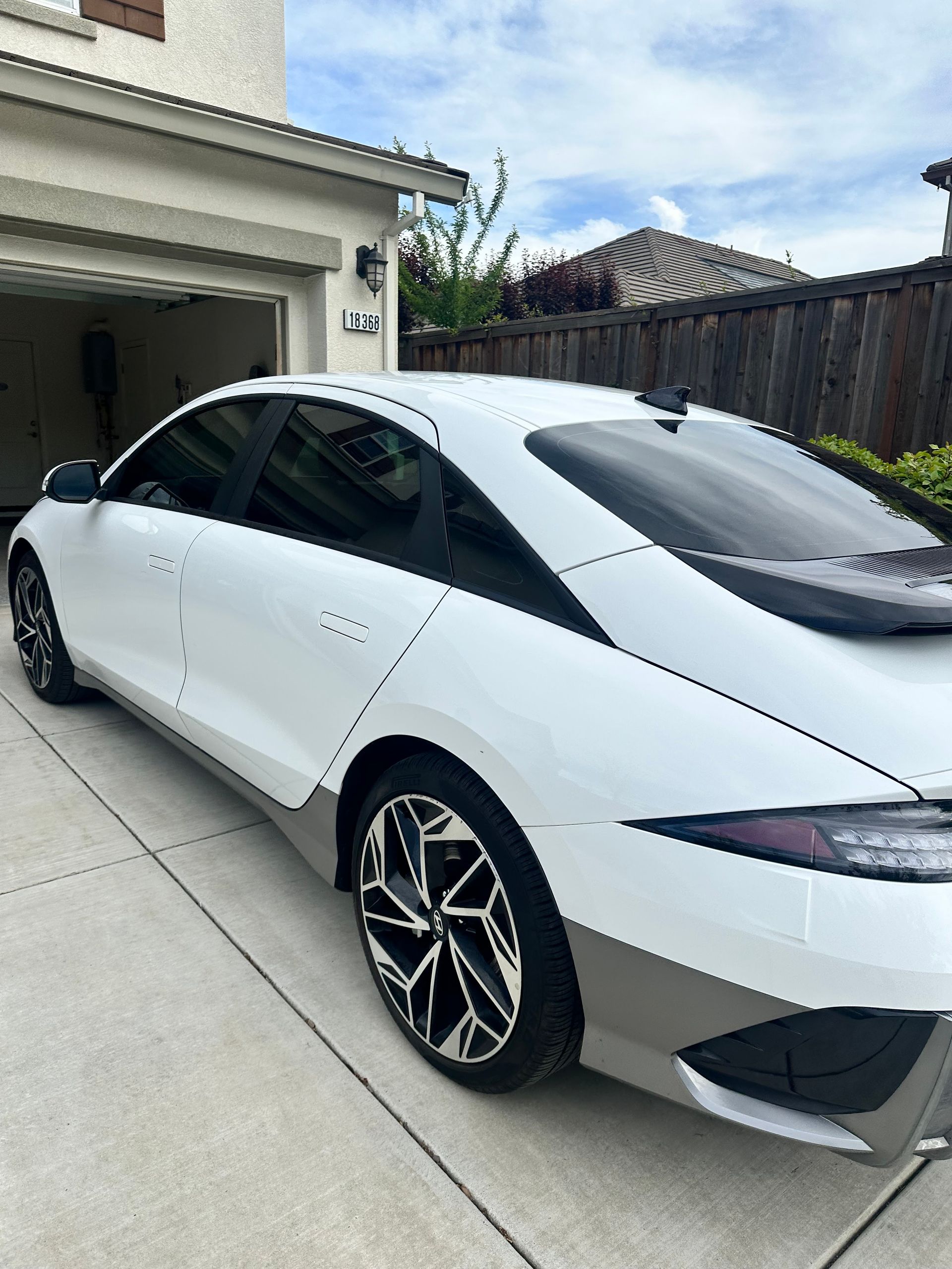 White sedan parked in a driveway beside a garage, viewed from the rear side.