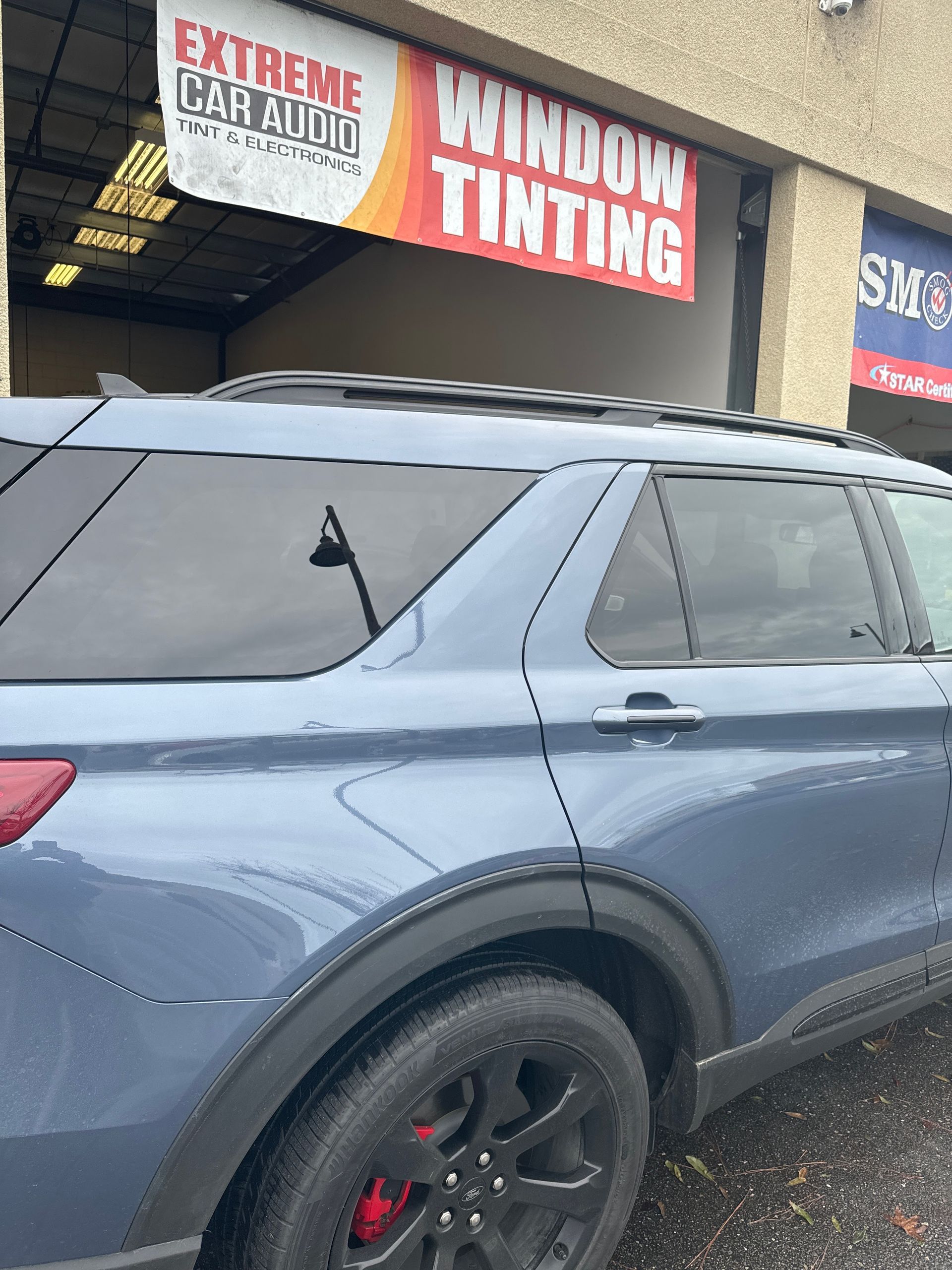 Blue SUV parked outside a window tinting shop with red signage.