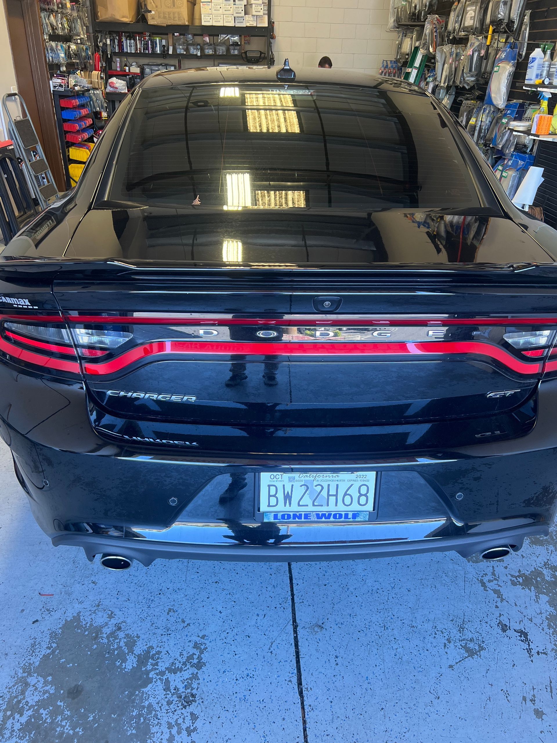 Black Dodge Charger seen from the rear in a garage, with red taillight strip and wet floor.