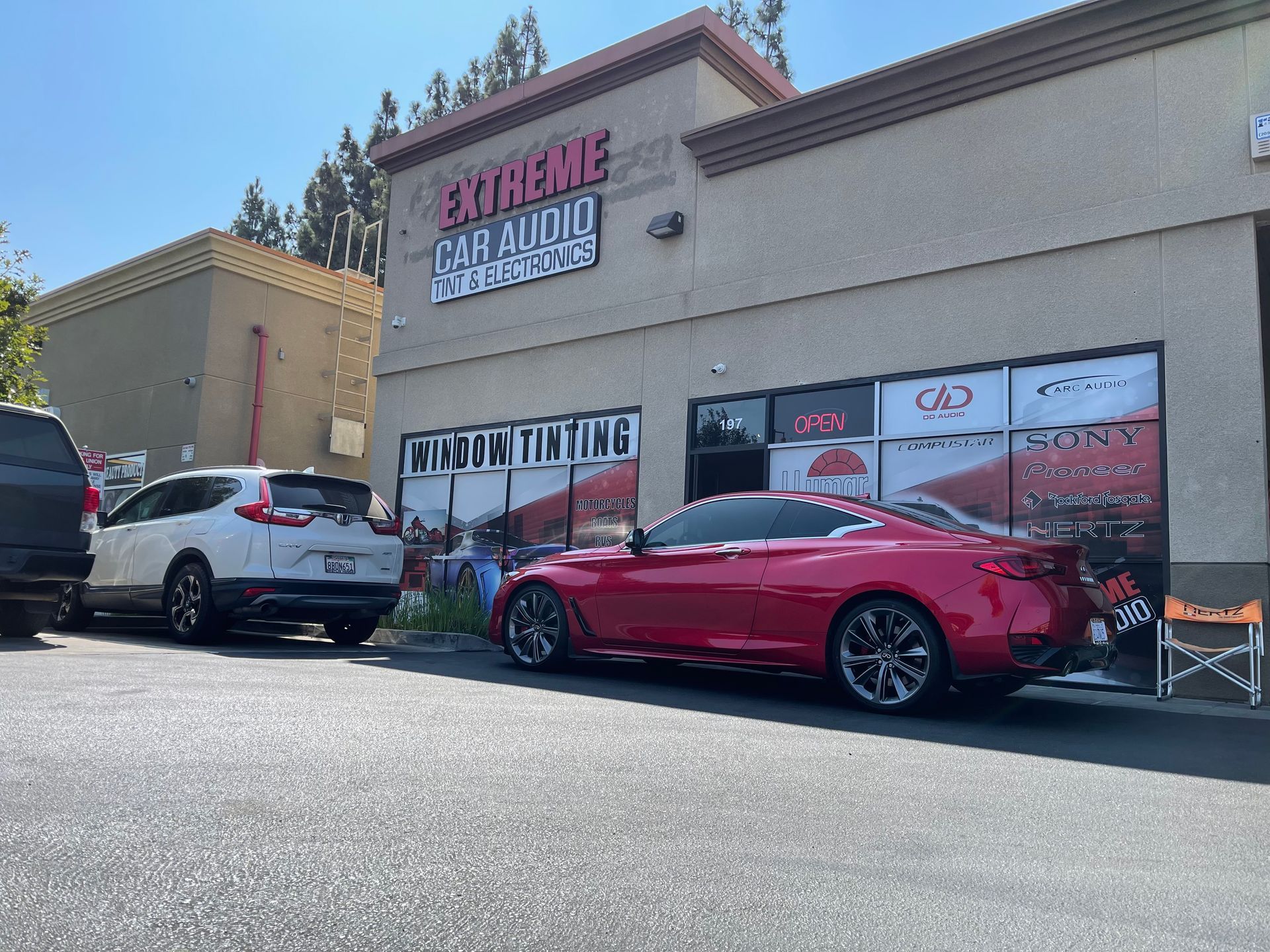 Red sports car parked outside a tire shop storefront on a sunny day.