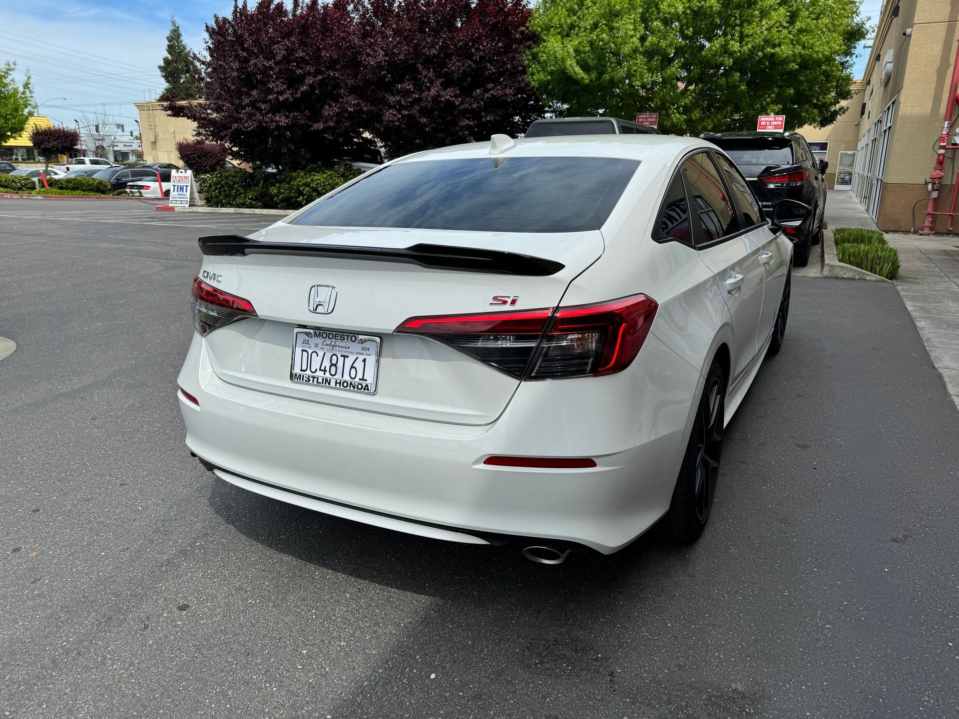White Honda sedan parked on a residential street beside a sidewalk and greenery.