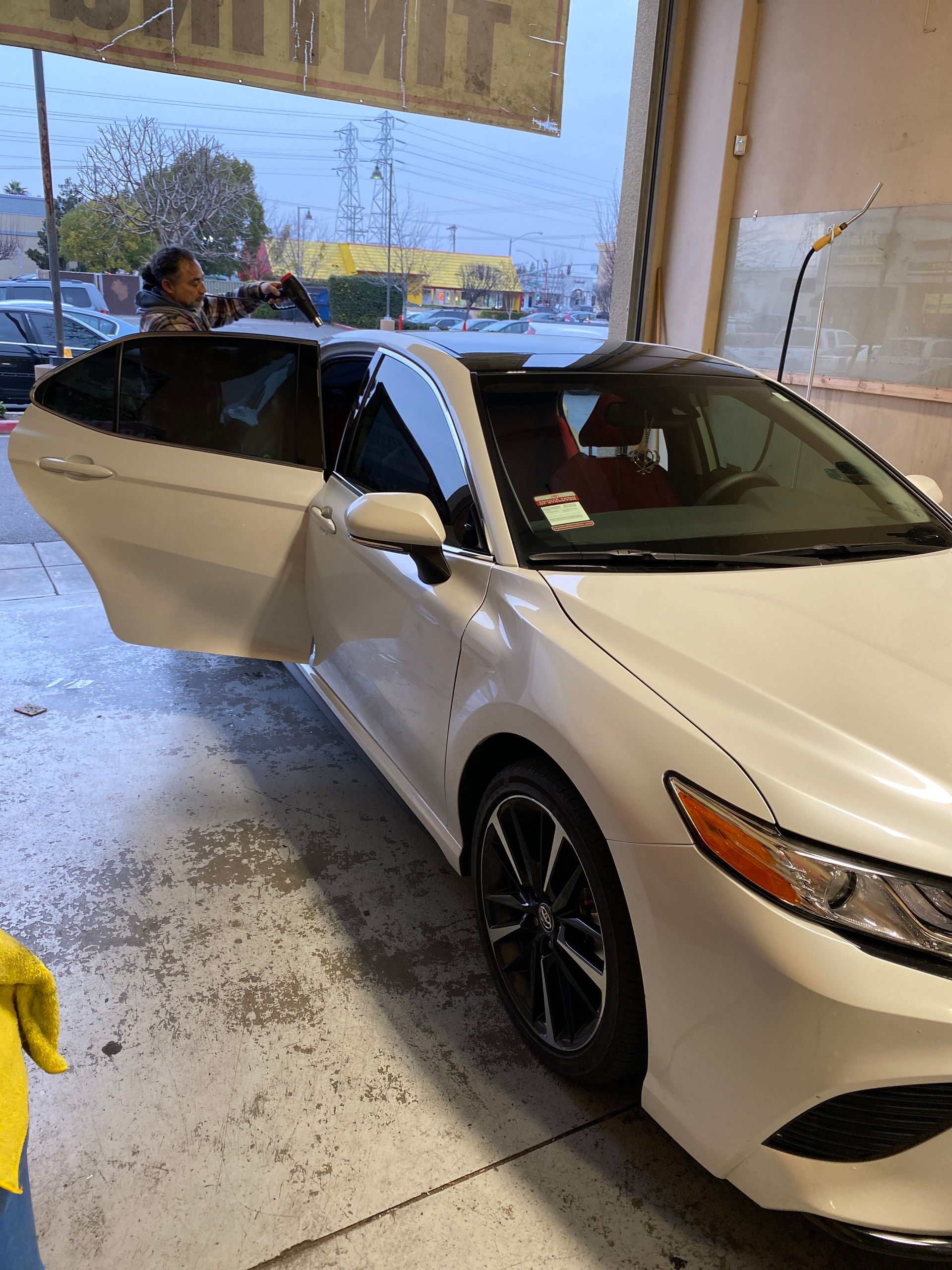 White sedan with open driver door inside a garage, front end visible.