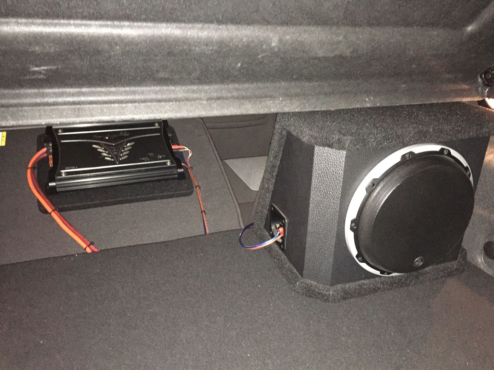 Small black device with orange wires mounted inside a vehicle compartment beside a round speaker or vent.