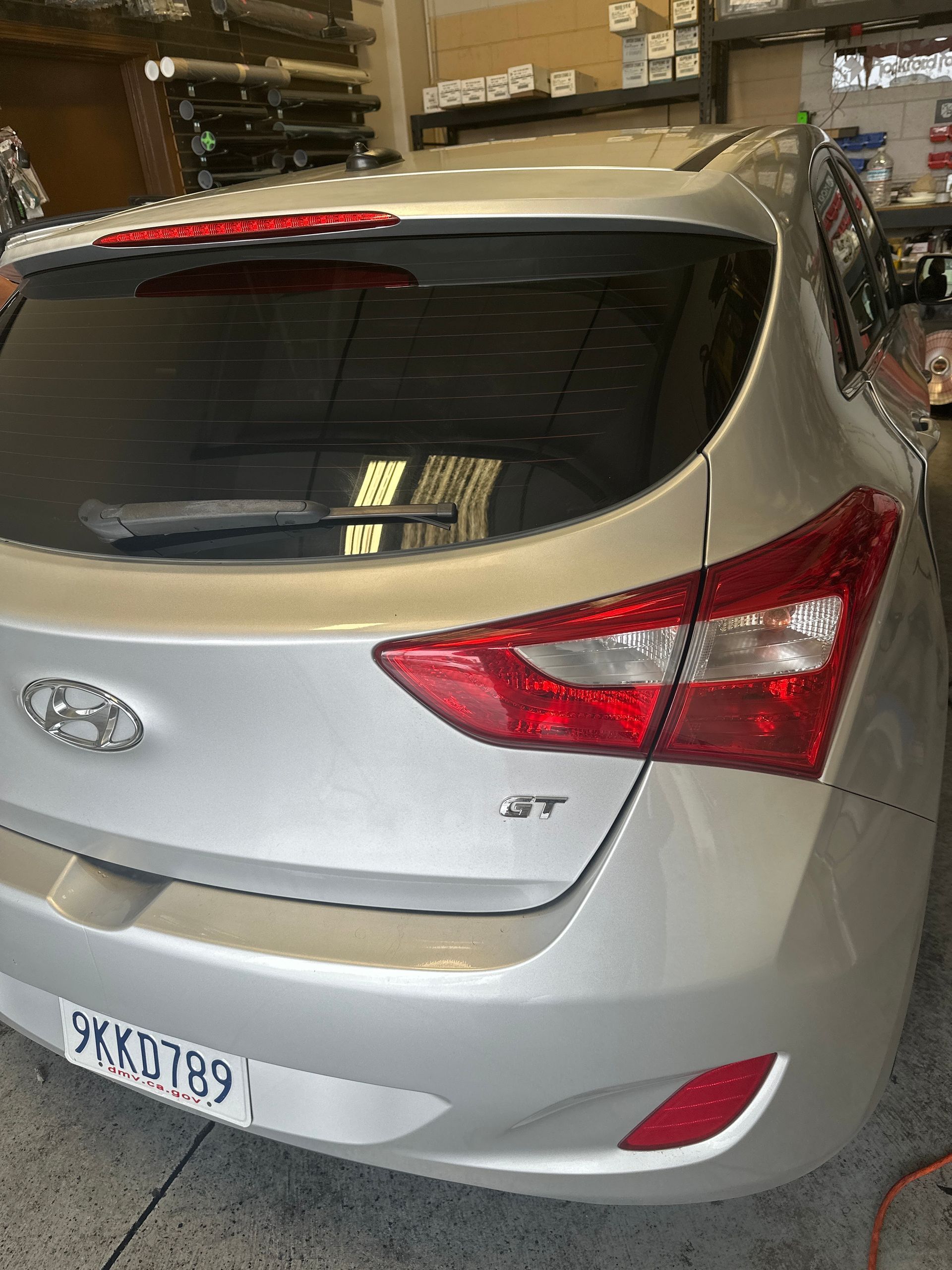 Silver Hyundai hatchback parked in a garage, rear view with visible taillights and license plate