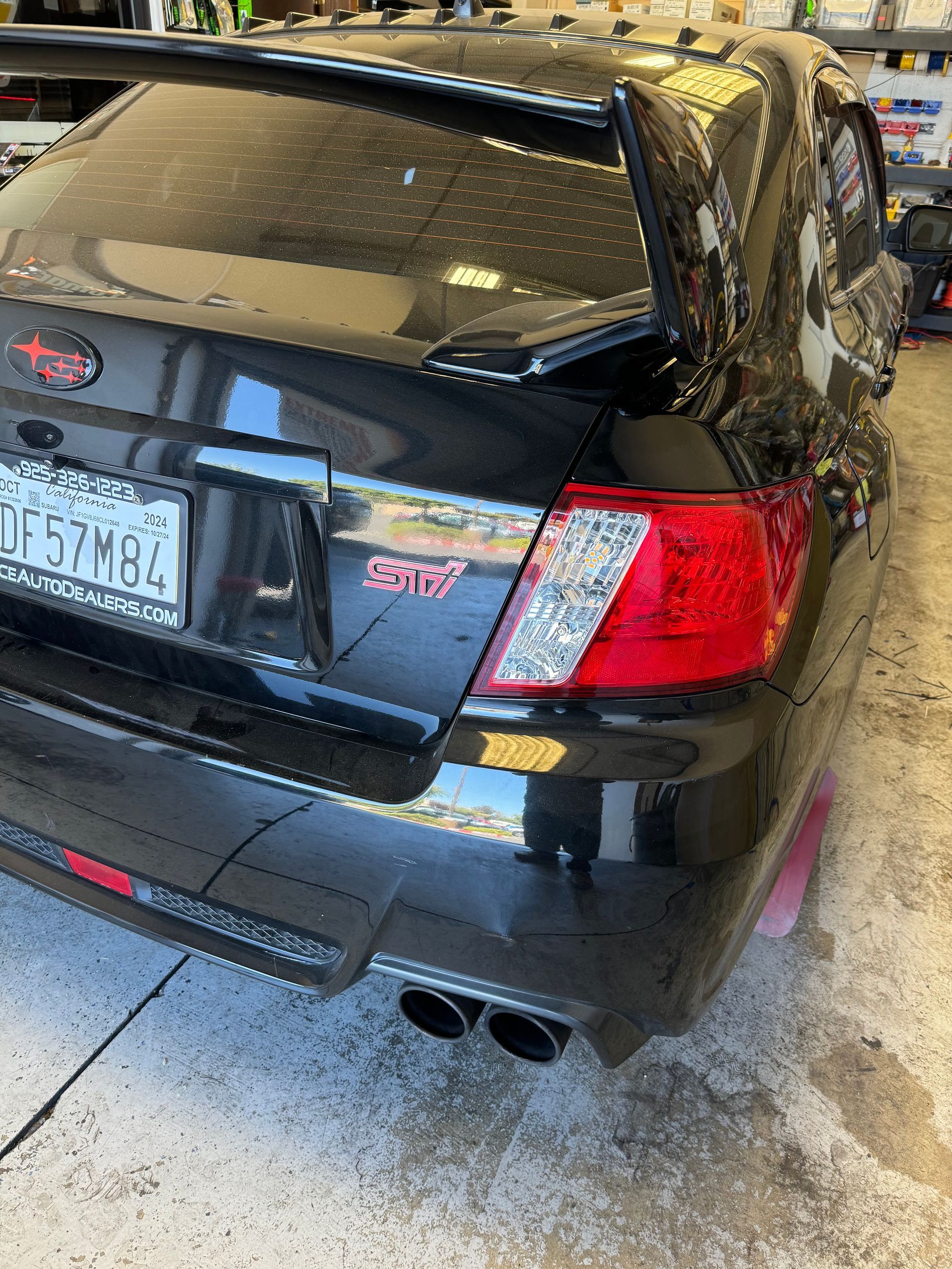 Black sedan parked in a snowy garage, rear view with visible taillights and exhaust pipes
