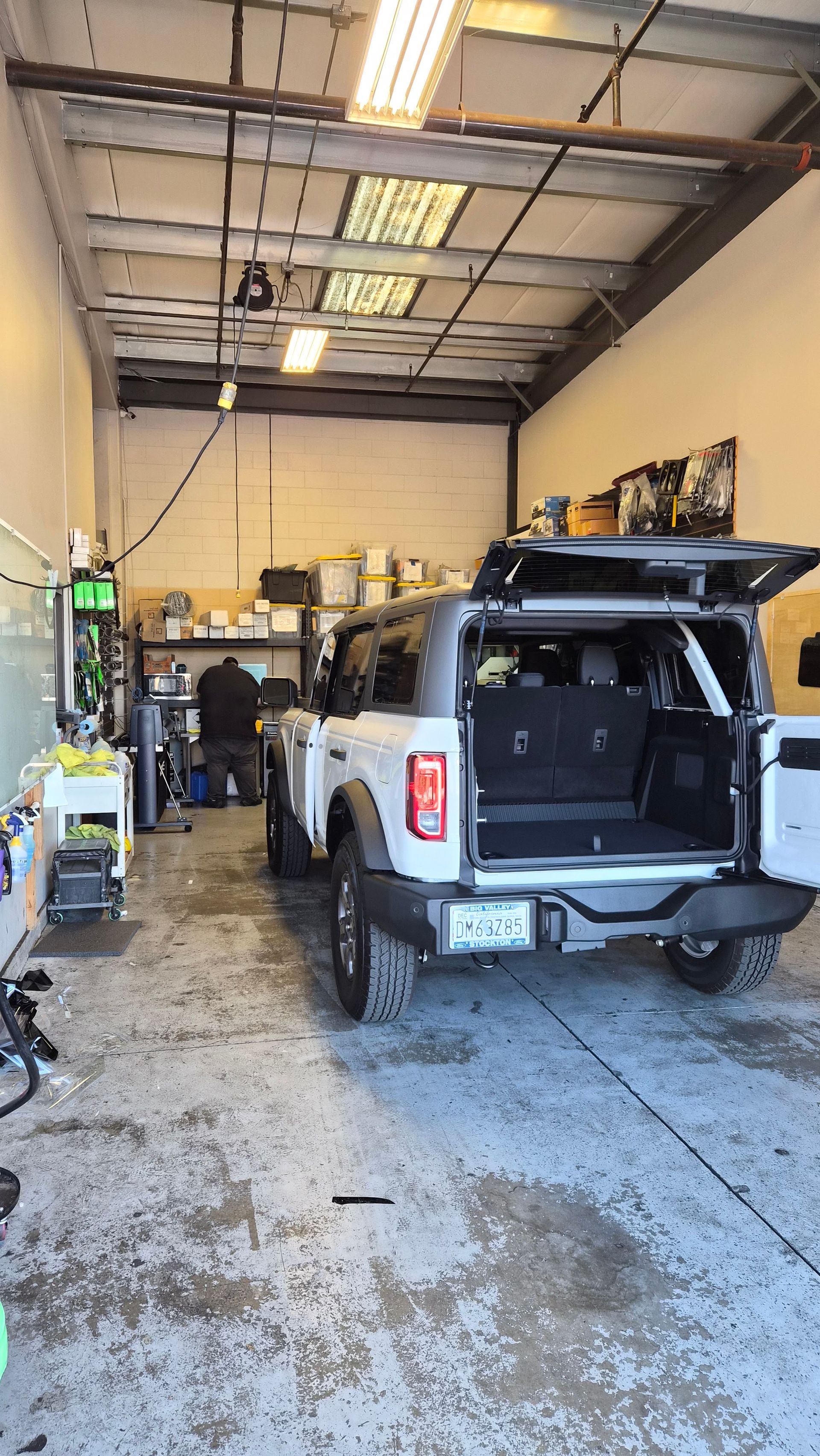 Auto repair garage with a white SUV, open rear hatch, and tools/workbenches inside.