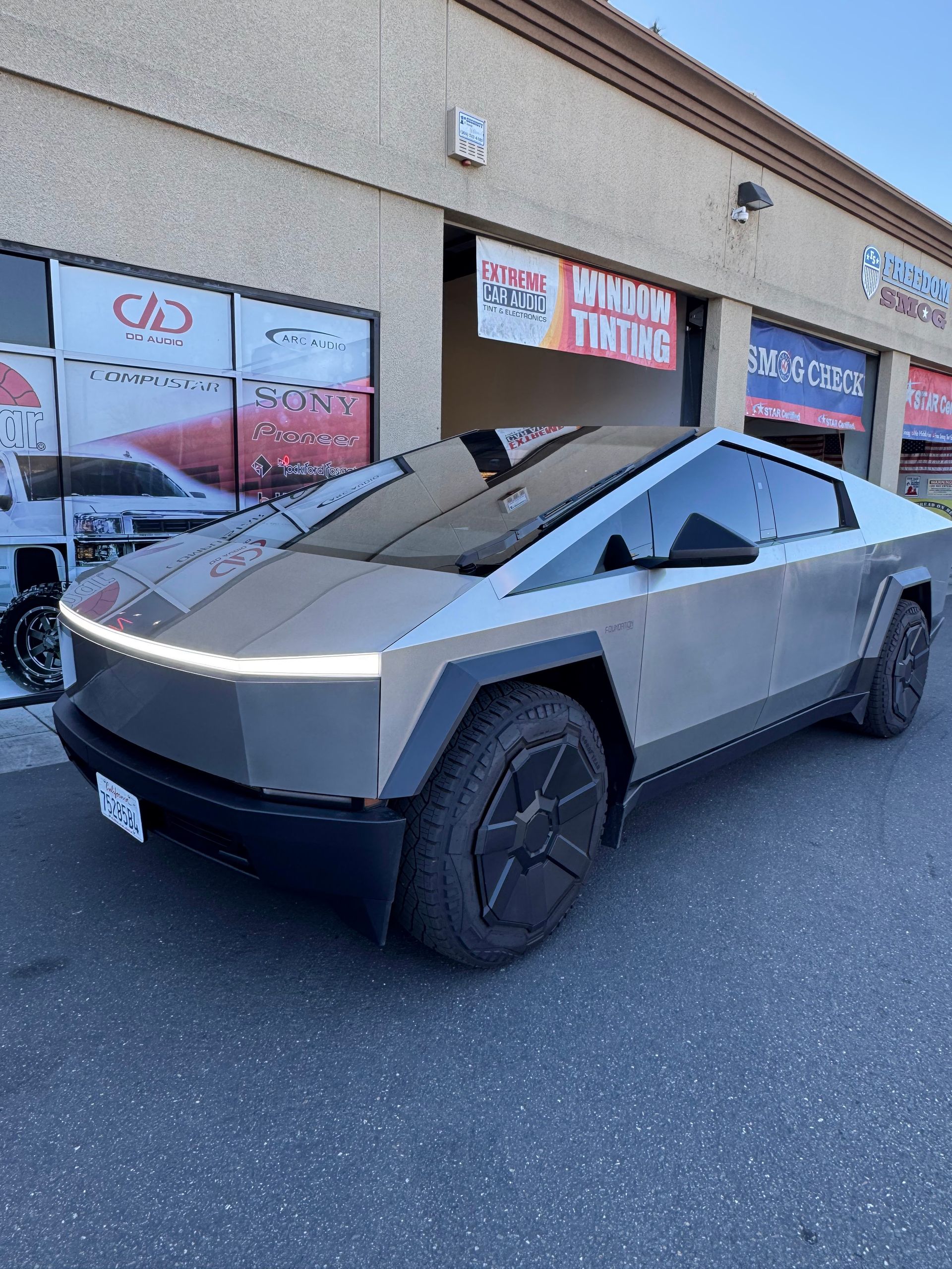 Silver Tesla Cybertruck parked outside a storefront in a parking lot.