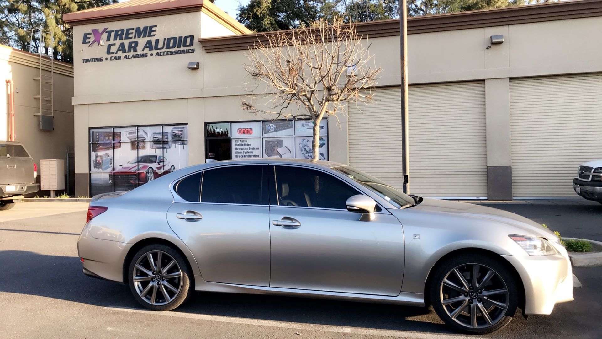 Silver sedan parked outside an Extreme Car Audio shop.