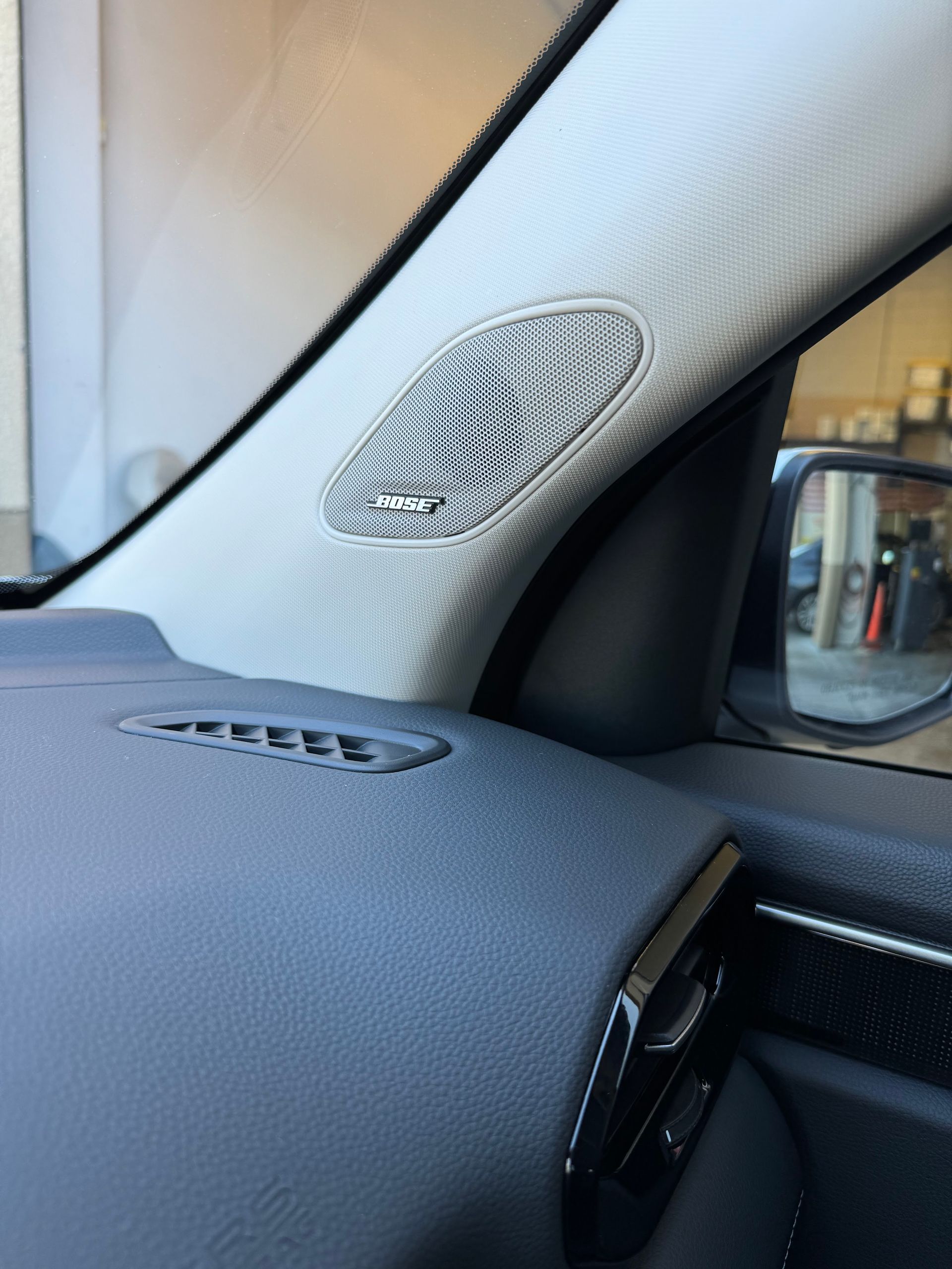 Close-up of a car dashboard and A-pillar speaker grille with a patterned white fabric trim.