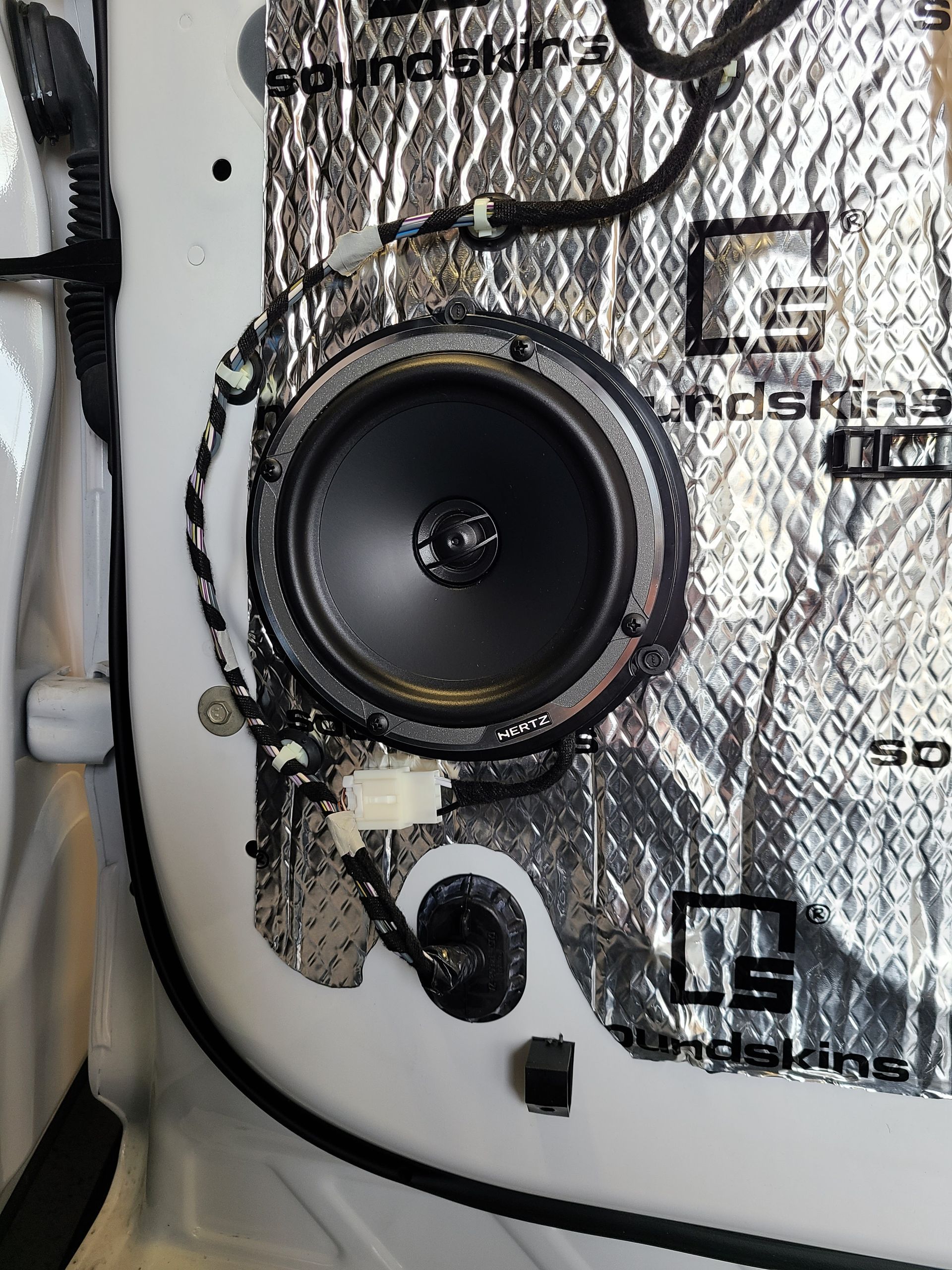 Close-up of a round black speaker mounted on a silver insulated panel with wires nearby
