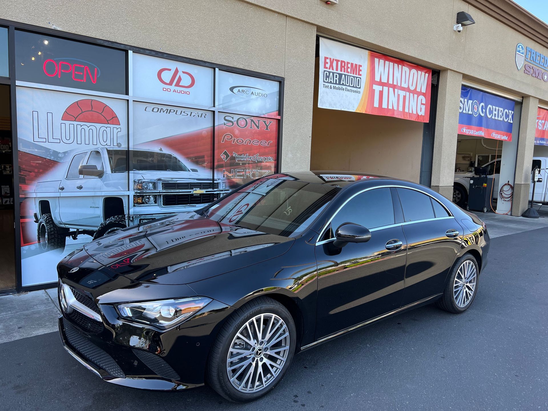 Black sedan parked outside a window-tinting shop with red-and-white signage