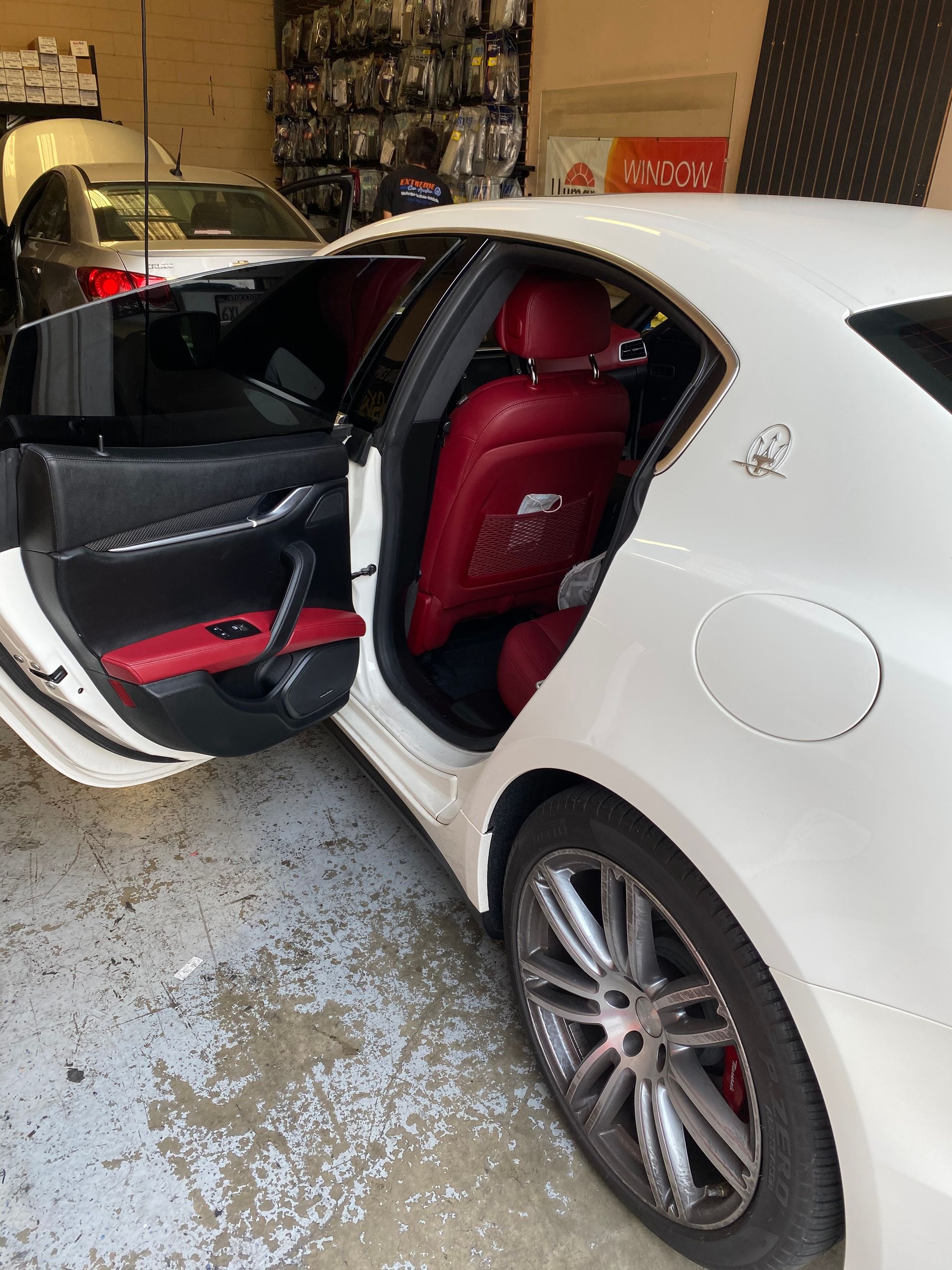White sedan with rear door open, showing red-and-black interior in a garage