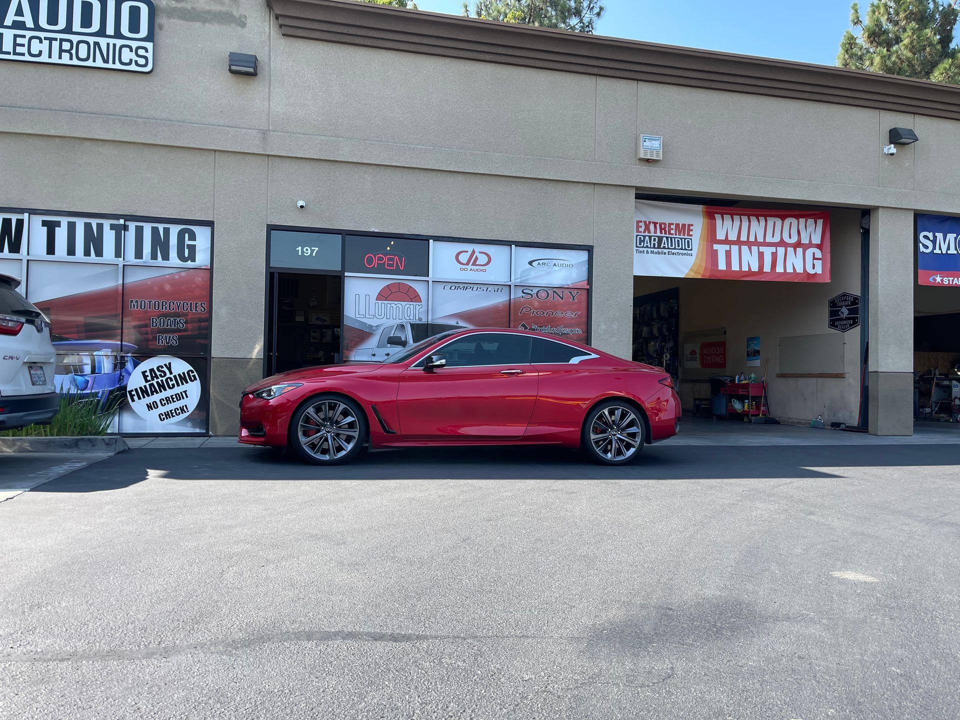Red sports car parked outside a tinting shop strip mall