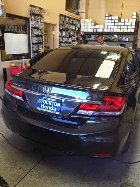 Black sedan in an auto shop, rear view, with a Stockton Honda license plate frame.