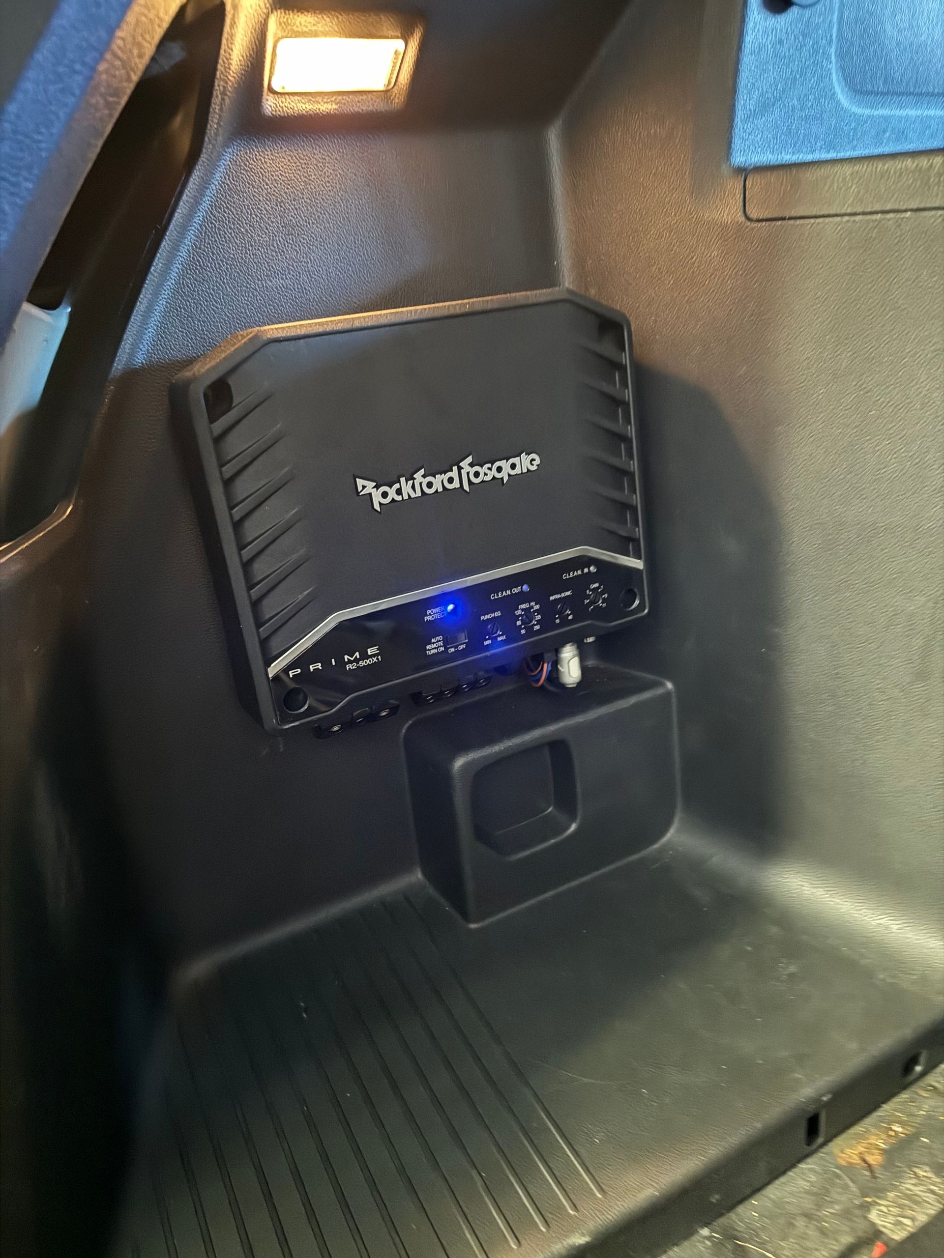 Black car seat back with a small blue-lit device clipped to it and a cupholder below.