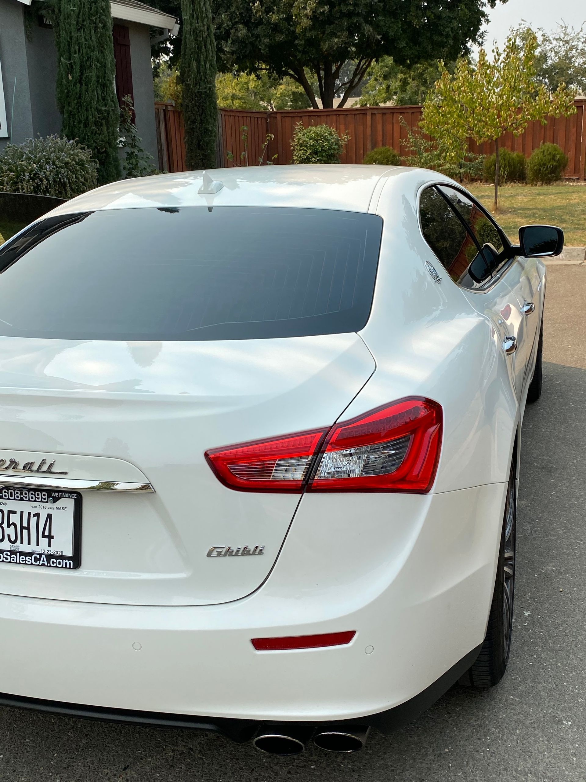 White sedan parked on a residential street, rear view with tinted windows and red taillights.