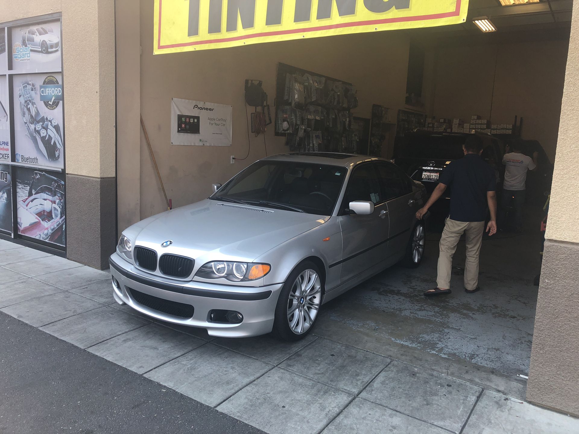 Silver BMW parked at a tire shop entrance, with a person standing beside it