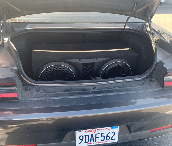 Open car trunk with two large subwoofers installed in the rear of a black car.