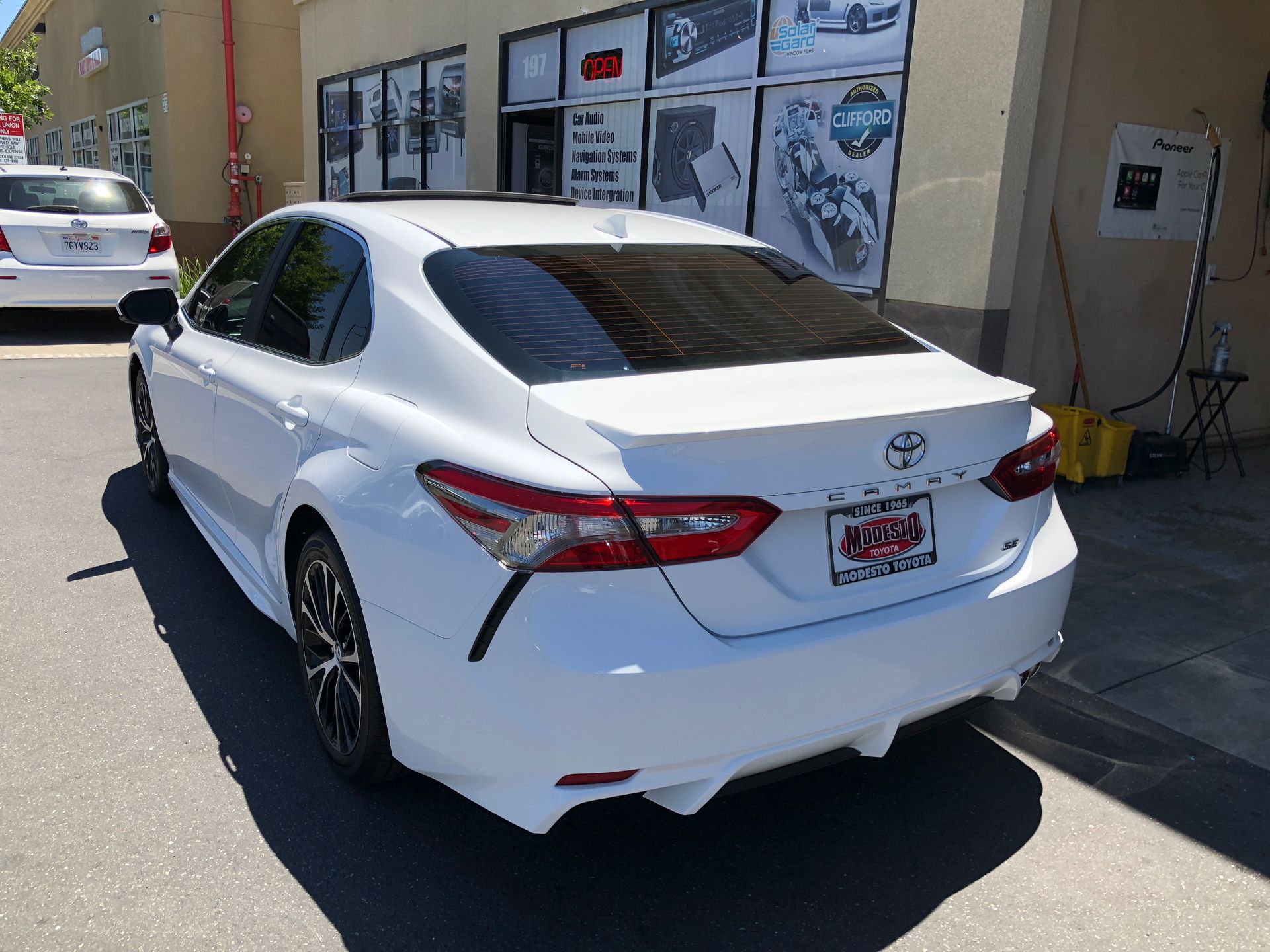 White Toyota sedan parked outside a building with wall-mounted displays.
