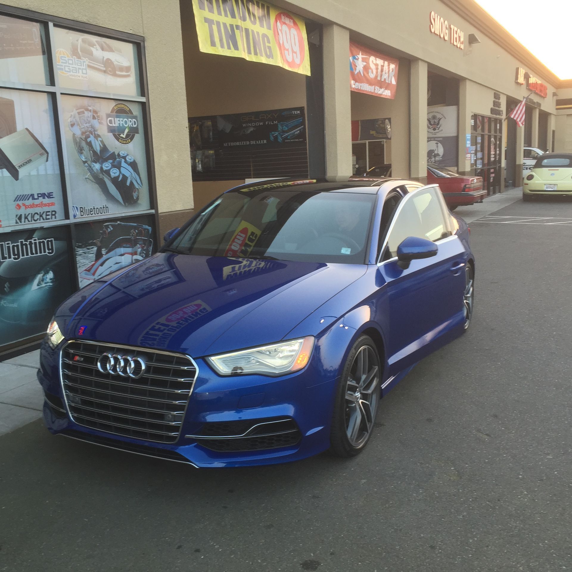 Blue Audi sedan parked outside a storefront in a strip mall parking lot