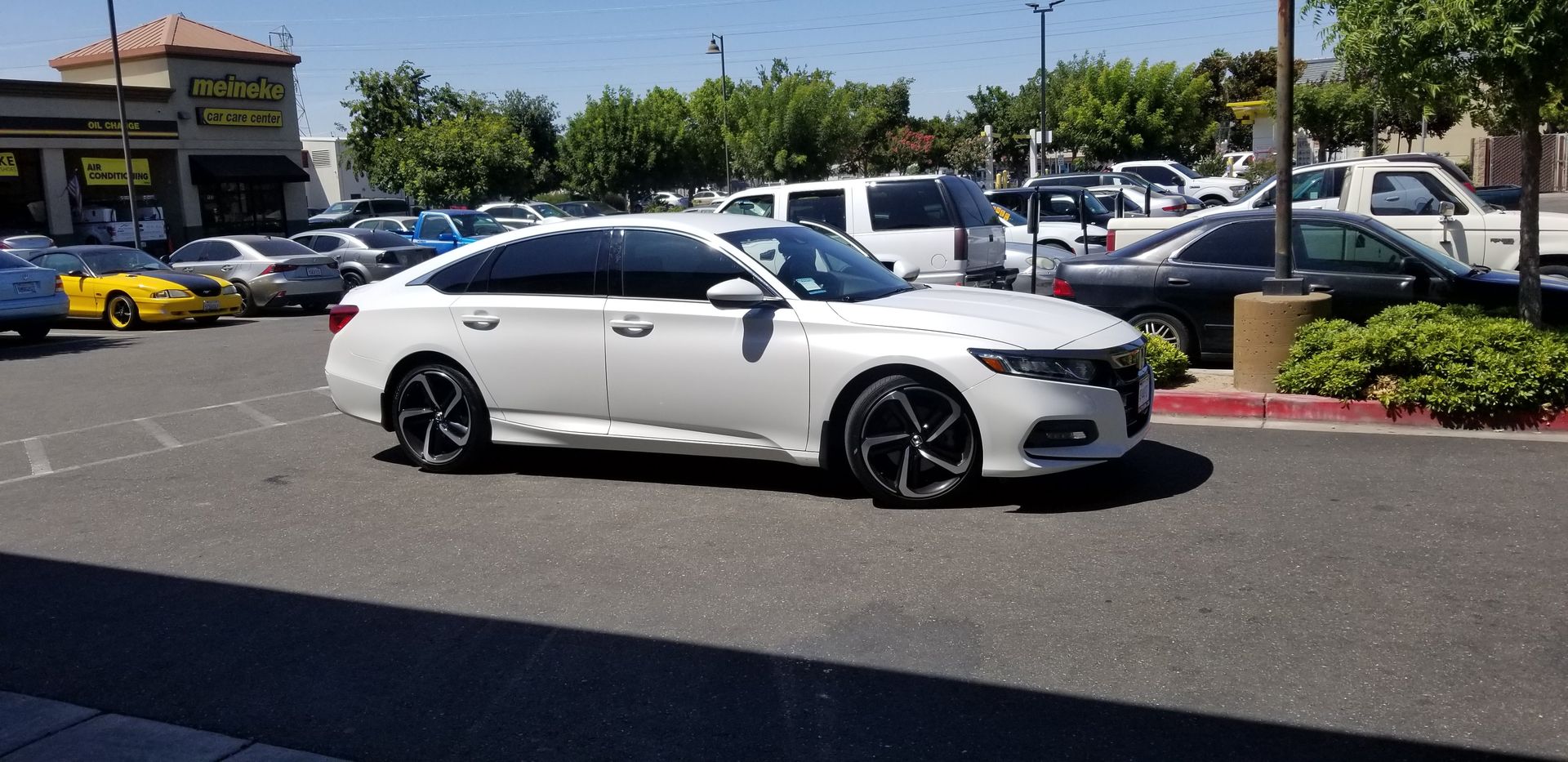 White sedan parked in a sunny lot with other cars and a shopping center in the background