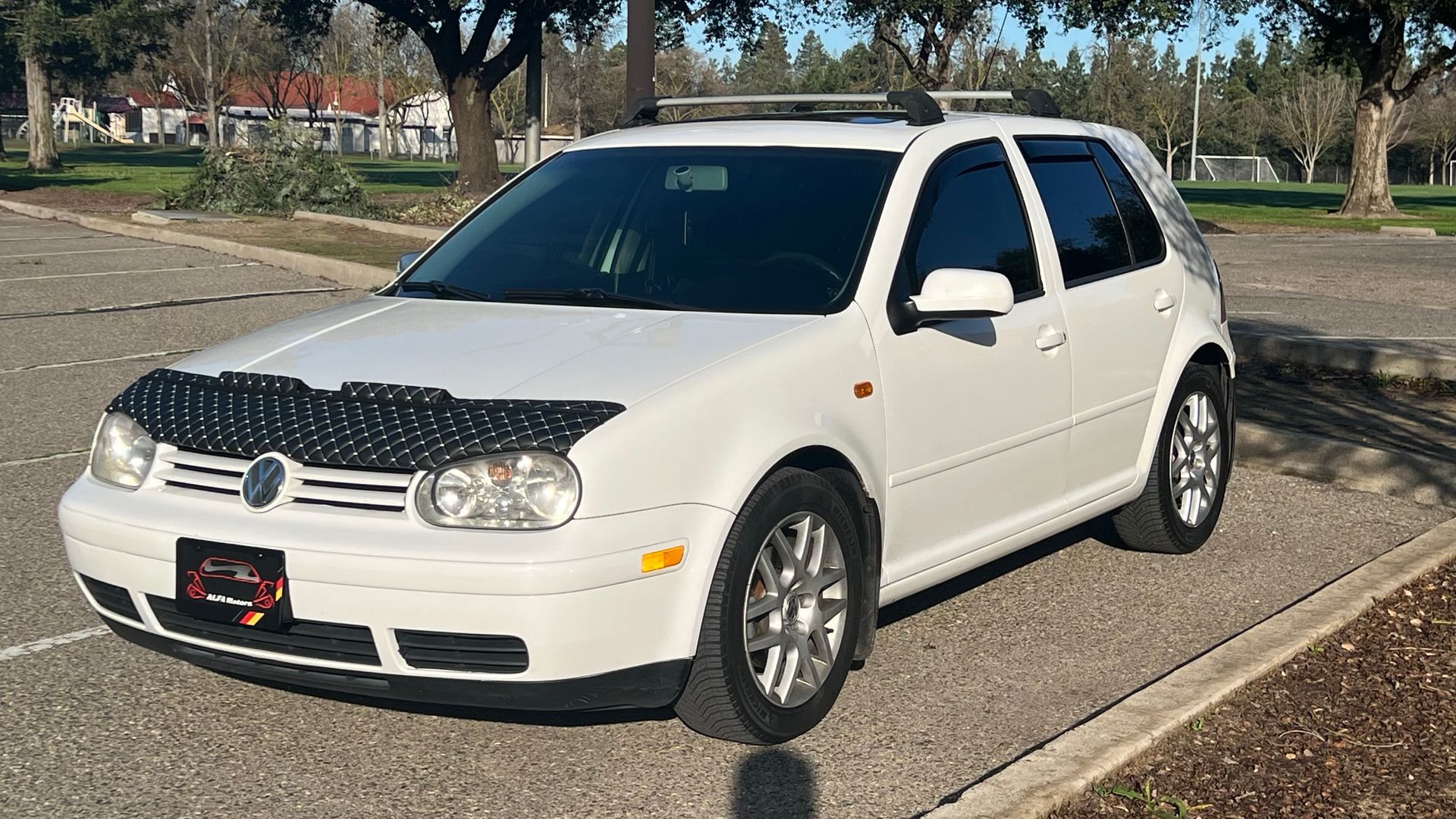 White compact SUV parked by a curb in a sunny park area, front-left view