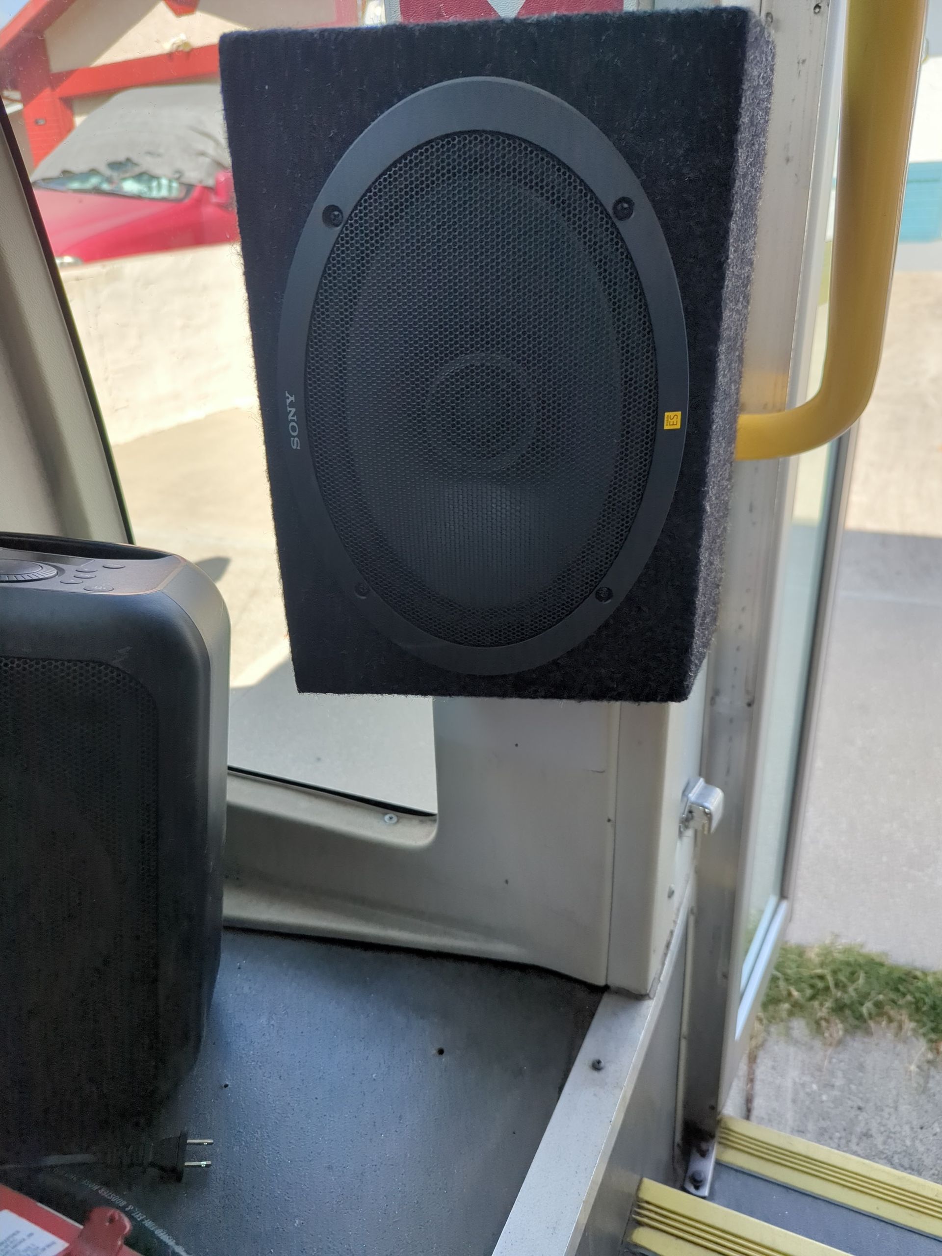 Black oval speaker mounted inside a bus near the door and window.