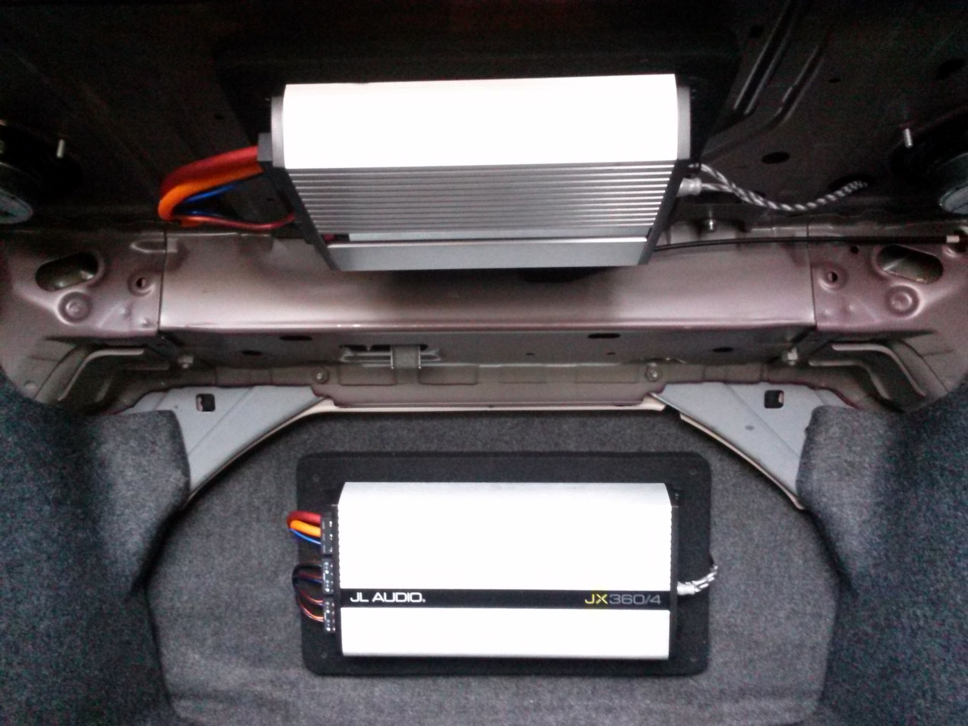 Two silver electronic modules mounted inside a car trunk, with red and black wires attached.