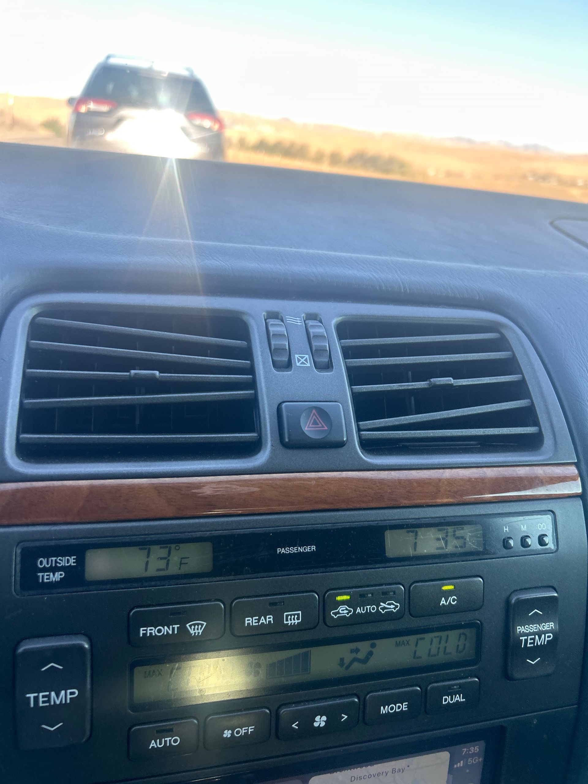 Car dashboard center console with vents and climate controls, looking out at a sunlit road ahead