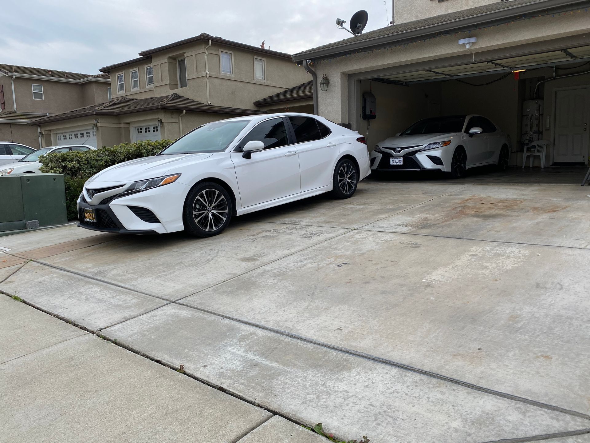 Two white sports cars parked in a driveway, one in a garage outside a suburban house.