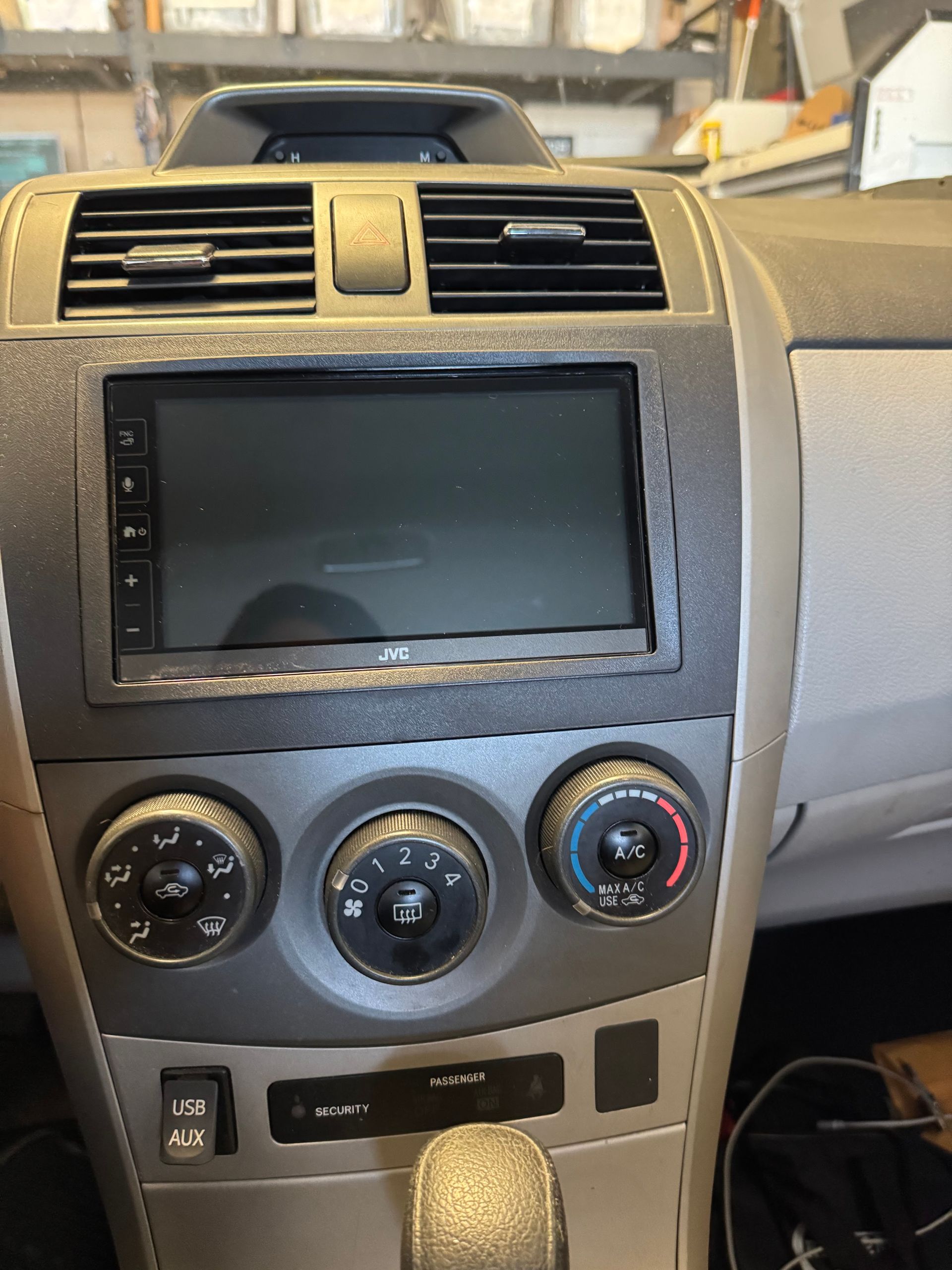 Car dashboard center console with touchscreen, air vents, and three climate control knobs in gray trim