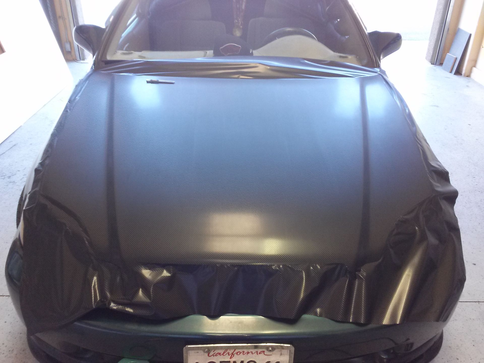 Damaged black car front end with crumpled hood and bumper in a garage