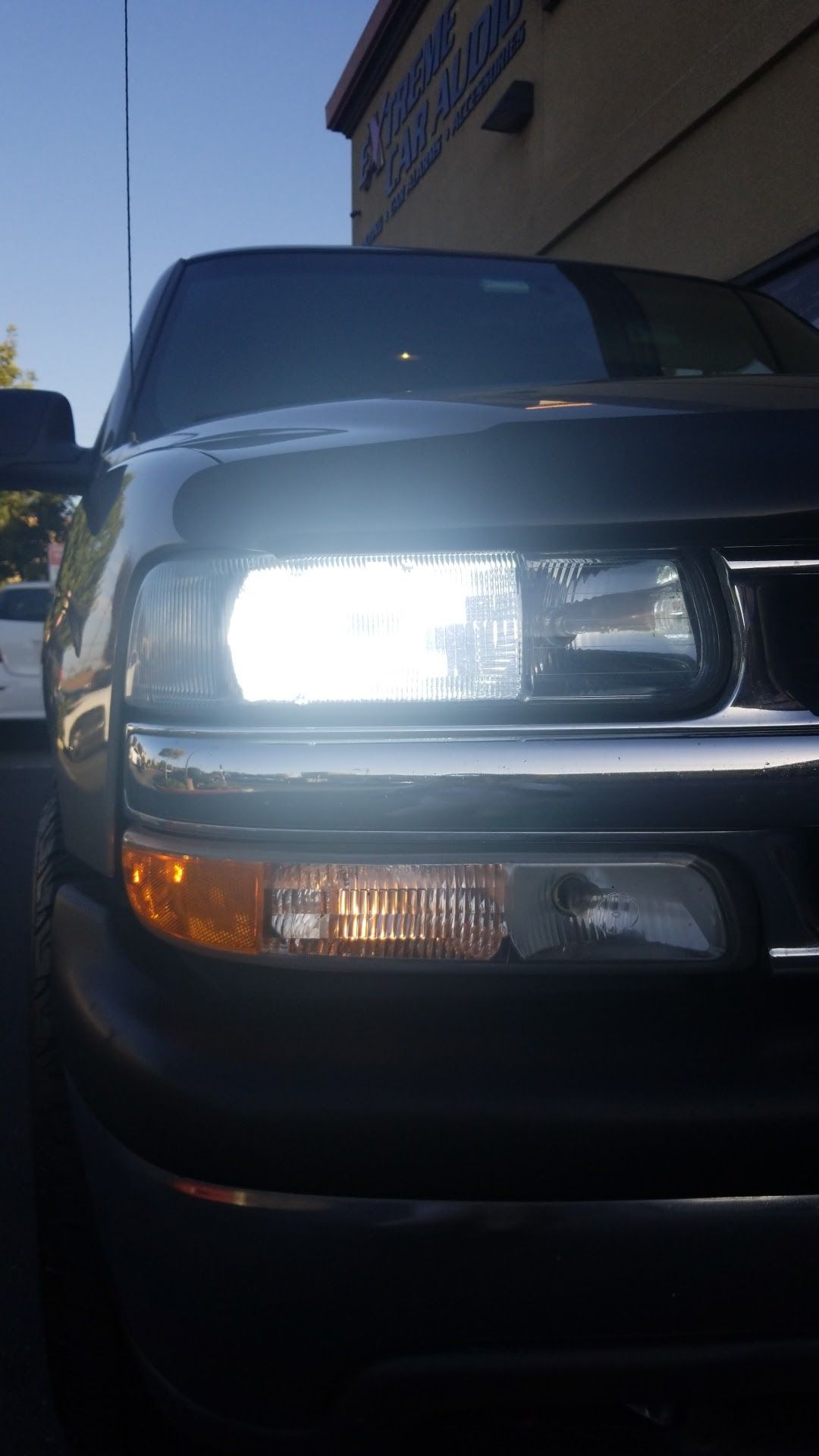 Front view of a black pickup truck with bright headlights parked beside a building.