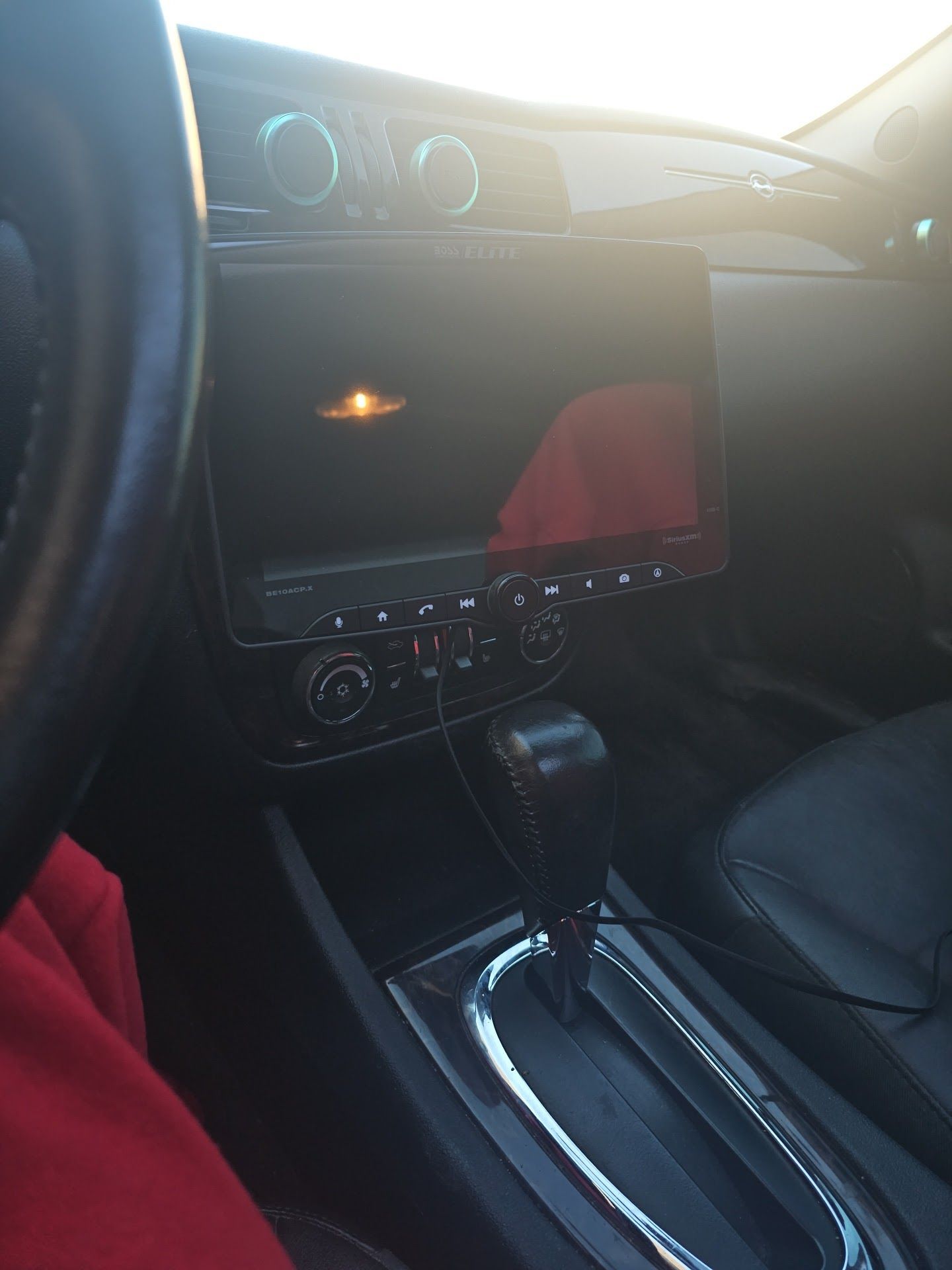 Car interior with center console, touchscreen display, gear shift, and steering wheel in sunlight