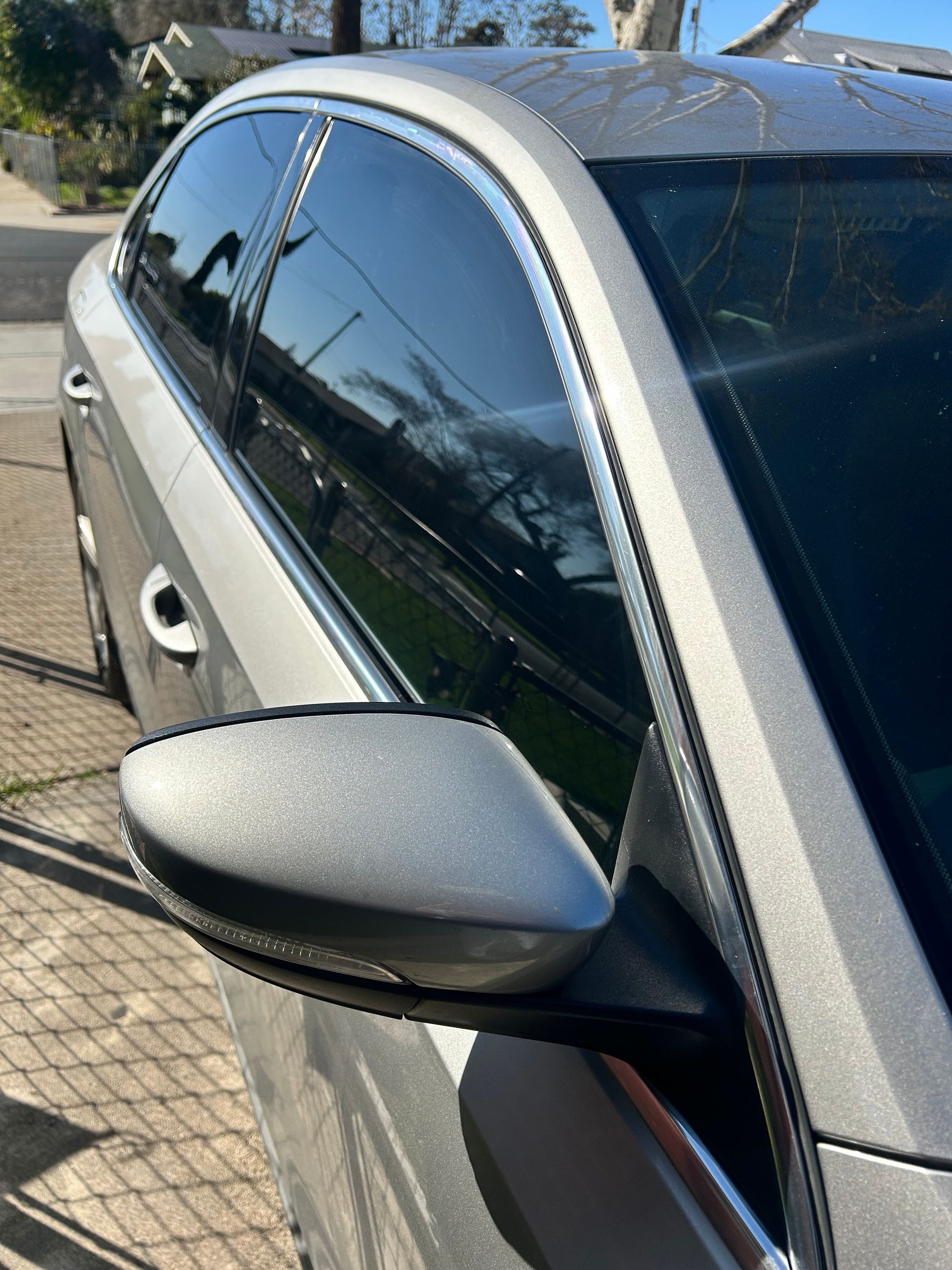 Silver car side mirror and tinted window in sunlight on a residential street